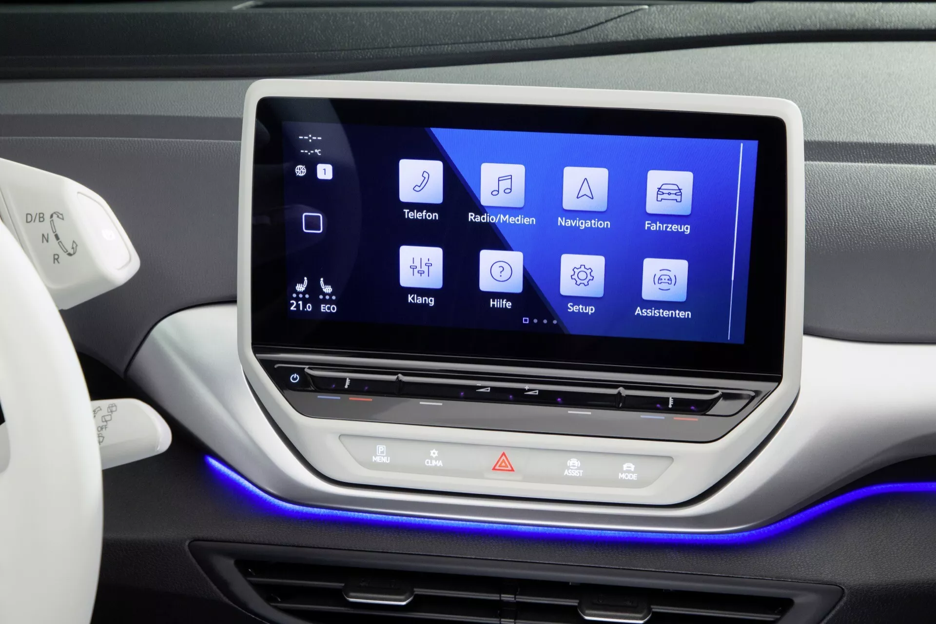 Centralna sekcja deski rozdzielczej VW ID.4 2020 z dużym systemem infotainment na dotykowym ekranie z ikonami do Telefonu, Radia/Mediów, Nawigacji, Ustawień pojazdu, Ustawień dźwięku, Pomocy, Ustawień i Asystentów; wyposażona w fizyczne przyciski i centralny pokrętło pod ekranem, oświetlenie ambientowe i wskazanie kontroli klimatu