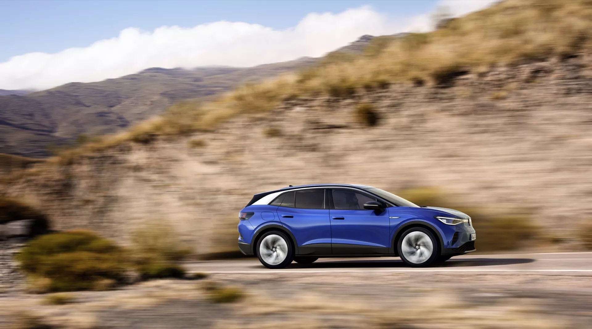Volkswagen ID.4 1. generacji 2020 w dynamicznym widoku bocznym prezentujący zaawansowane cechy technologiczne, reflektory LED i aerodynamiczny design na tle zamazanego krajobrazu naturalnego, podkreślający jego zdolność do radzenia sobie z różnymi terenami.