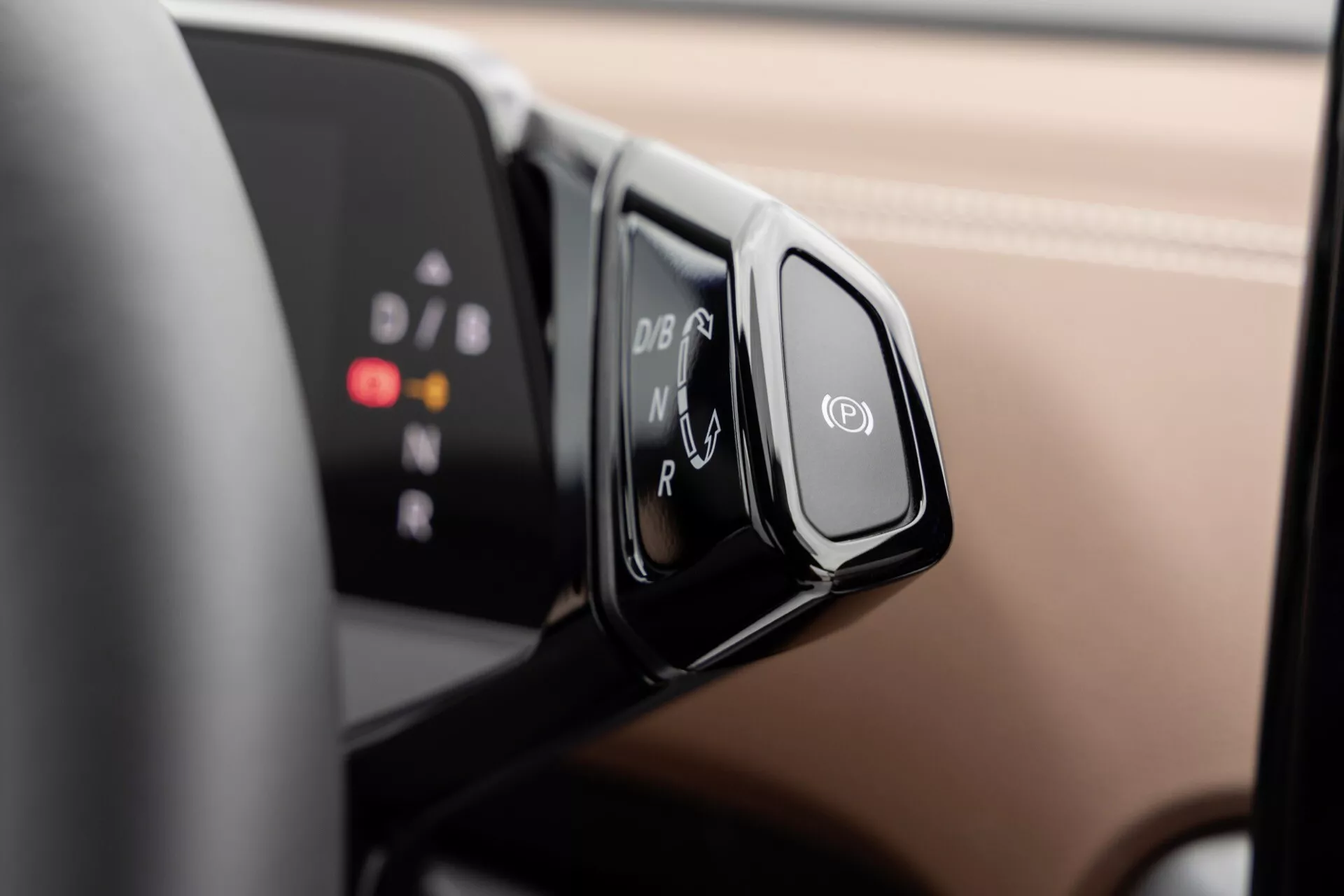 Zbliżenie na wybierak zmiany biegów VW ID.4 2020 o ergonomicznym wzornictwie i systemie shift-by-wire, wyświetlający tryby P, R, N, D, B na czarnym panelu, zamontowany na kolumnie kierowniczej, z rozmazanym cyfrowym wyświetlaczem deski rozdzielczej w tle