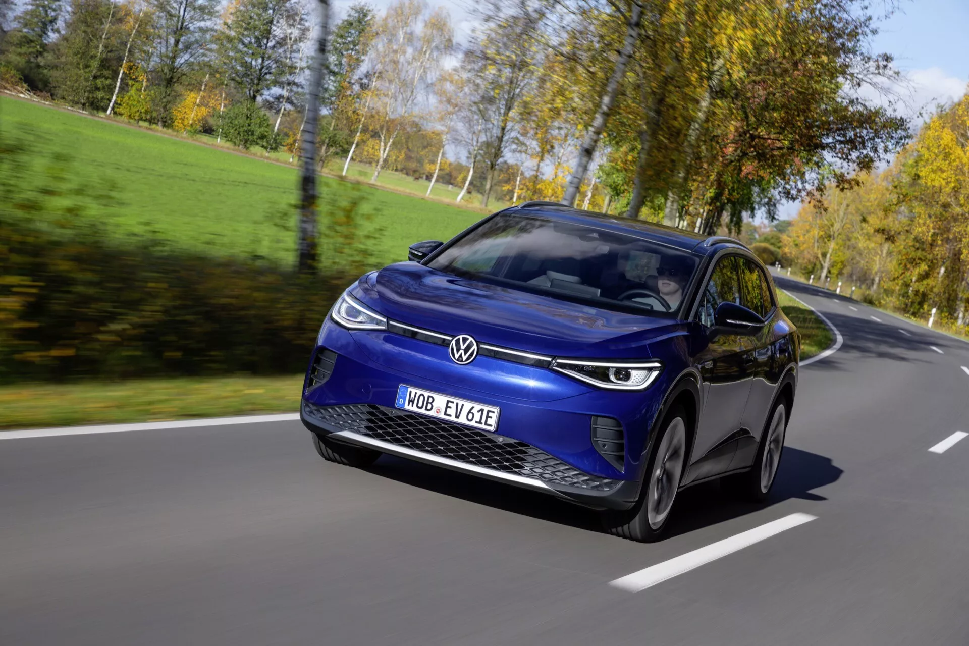Dynamiczny widok z przodu trzy czwarte Volkswagen ID.4 1. generacji z 2020 roku w ruchu w jasny dzień, prezentuje jego aerodynamiczny niebieski design hatchback, wyraziste światła LED, i zaawansowane funkcje technologiczne, w tym cyfrowy wyświetlacz i oznaczenie pojazdu elektrycznego