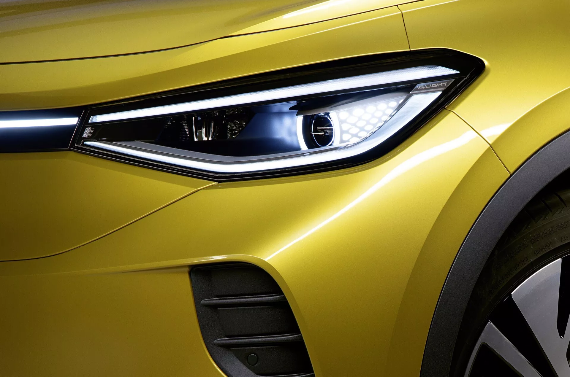 Zbliżony widok na przednią lewą sekcję VW ID.4 z roku 2020, podkreślający nowoczesny design reflektora LED, premium metaliczny żółty lakier i aerodynamiczne cechy nadwozia, w tym widoczną wlot powietrza