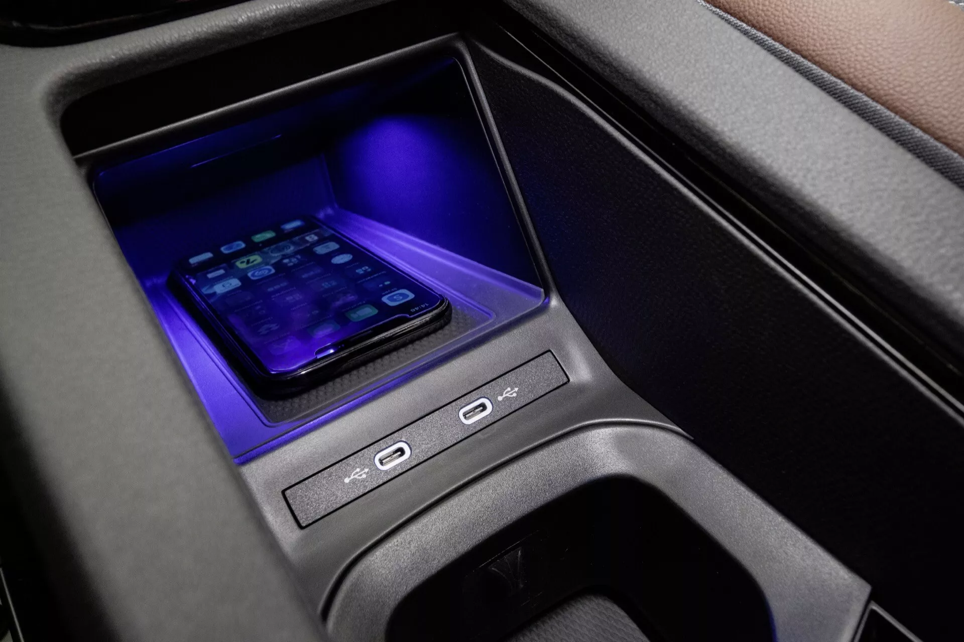 Zbliżenie na środkową konsolę VW ID.4 2020 pierwszej generacji z bezprzewodową stacją dokującą do smartfonów, niebieskim oświetleniem ambientowym, przyciskami sterowania oraz nowoczesną łącznością w wysokiej jakości wnętrzu