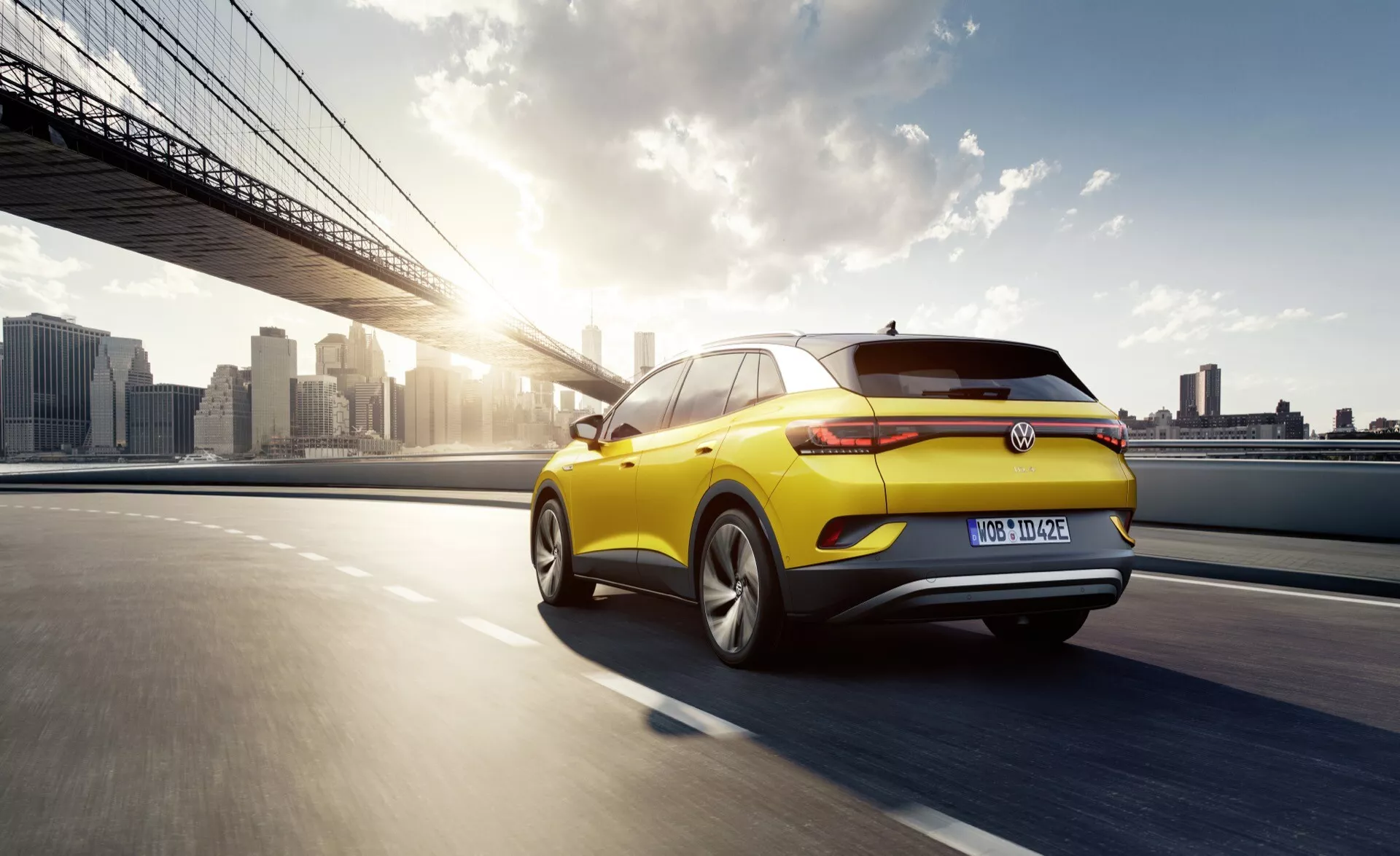 Dynamiczny widok z tyłu trzech czwartych żółtego hatchbacka Volkswagen w ruchu z tylnymi światłami LED, felgami z aluminium i aerodynamicznym designem na tle miejskiego zachodu słońca