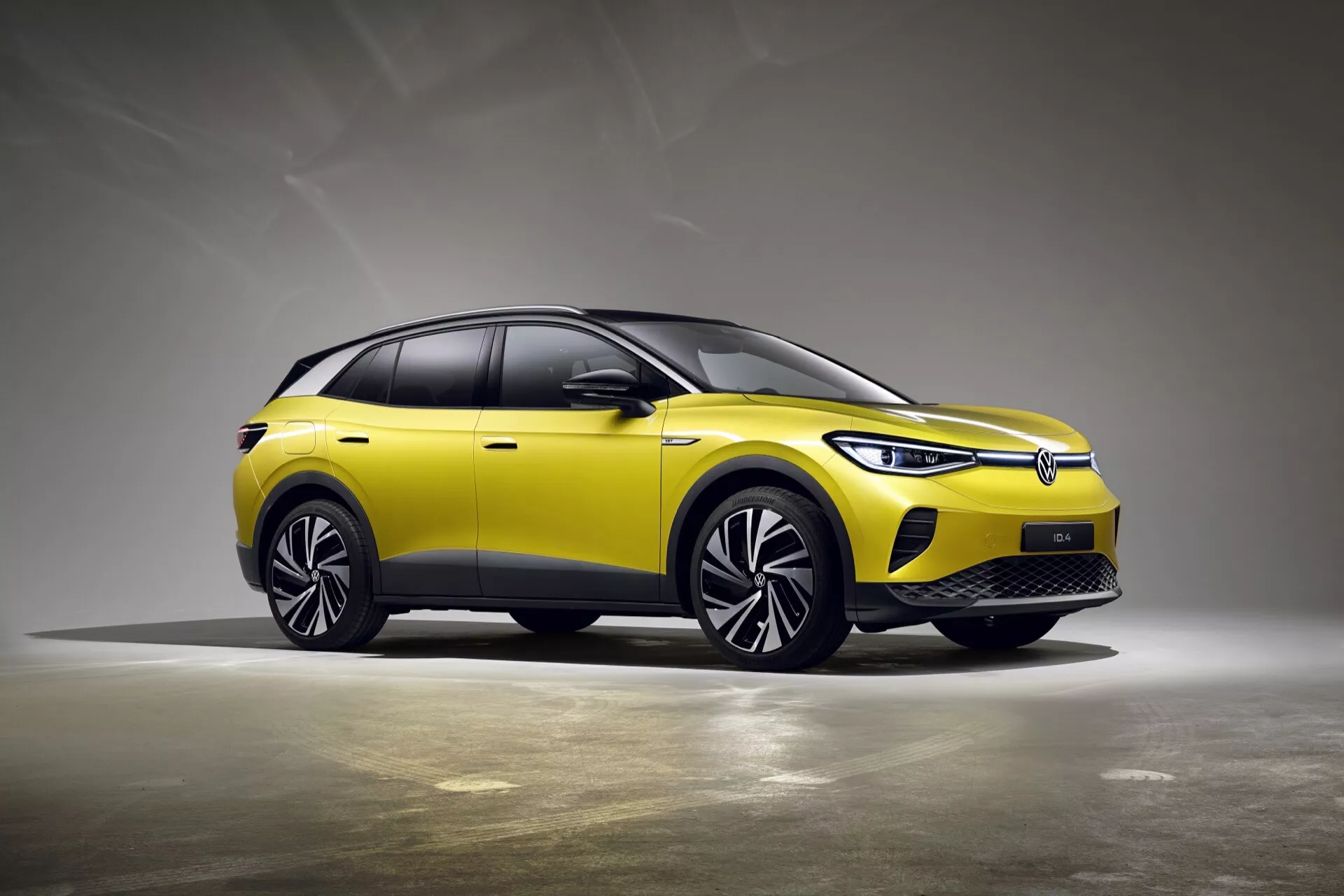 Widok z przodu trzy czwarte żółtego crossovera SUV VW ID.4 1. generacji 2020 na neutralnym szarym tle w studio, podkreślający jego zamkniętą kratę, reflektory LED, aerodynamiczne koła i eleganckie cechy konstrukcyjne