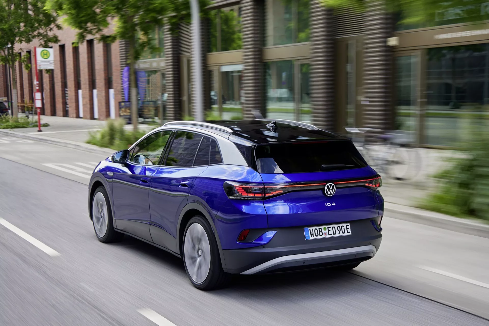 Dynamiczny widok z tyłu i prawej strony na niebieskiego Volkswagen ID.4, całkowicie elektrycznego SUV-a, w ruchu na miejskiej ulicy podkreślający jego prawy profil boczny, tylne światła LED i cechy aerodynamiczne z rozmyciem ruchu