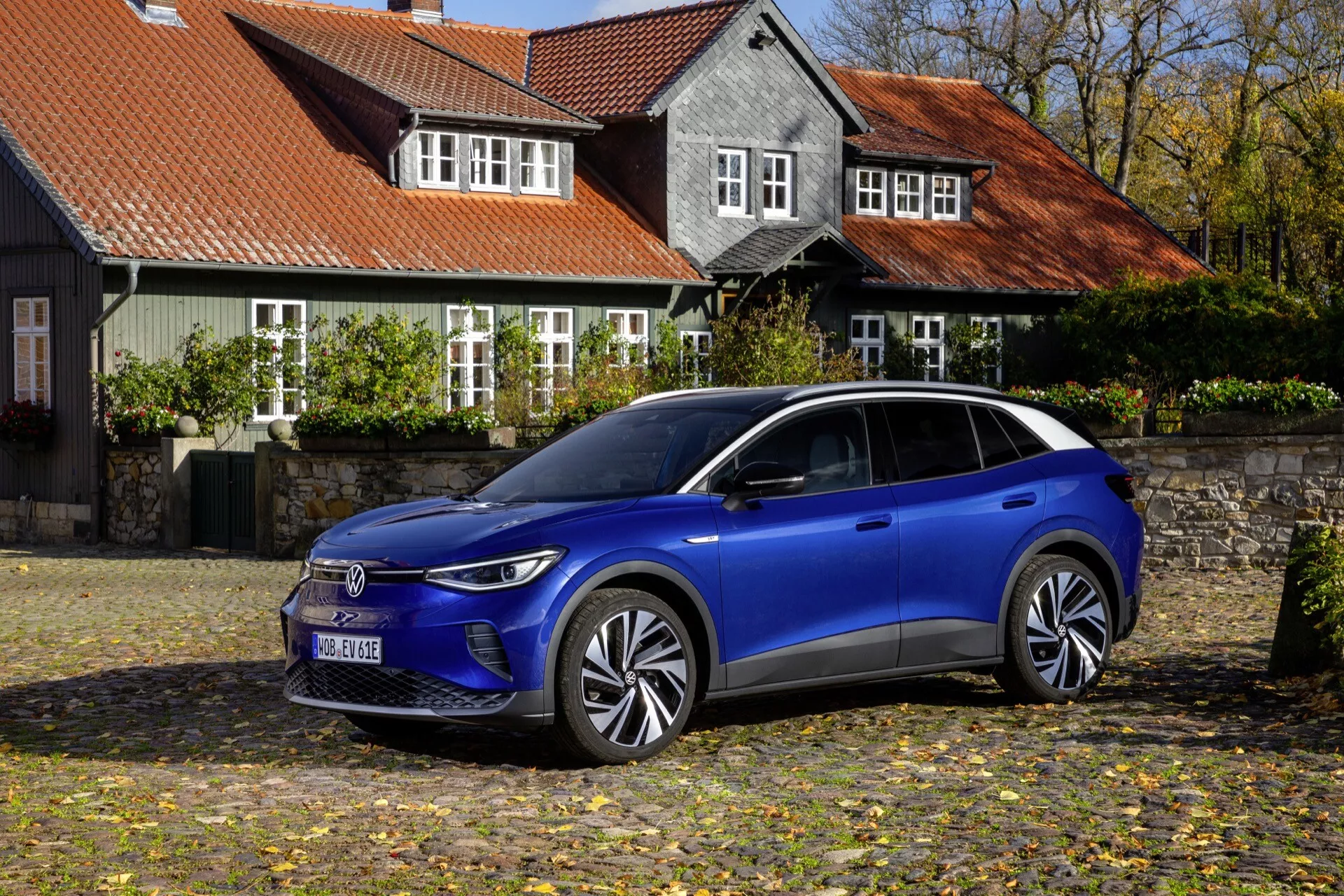 VW ID.4 1. generacji 2020 zaparkowany na bruku z jesiennymi liśćmi, podkreślający nowoczesny niebieski design elektrycznego SUV-a, zaawansowane reflektory LED, aerodynamiczne koła i potencjalne systemy wsparcia kierowcy w spokojnej historycznej okolicy.
