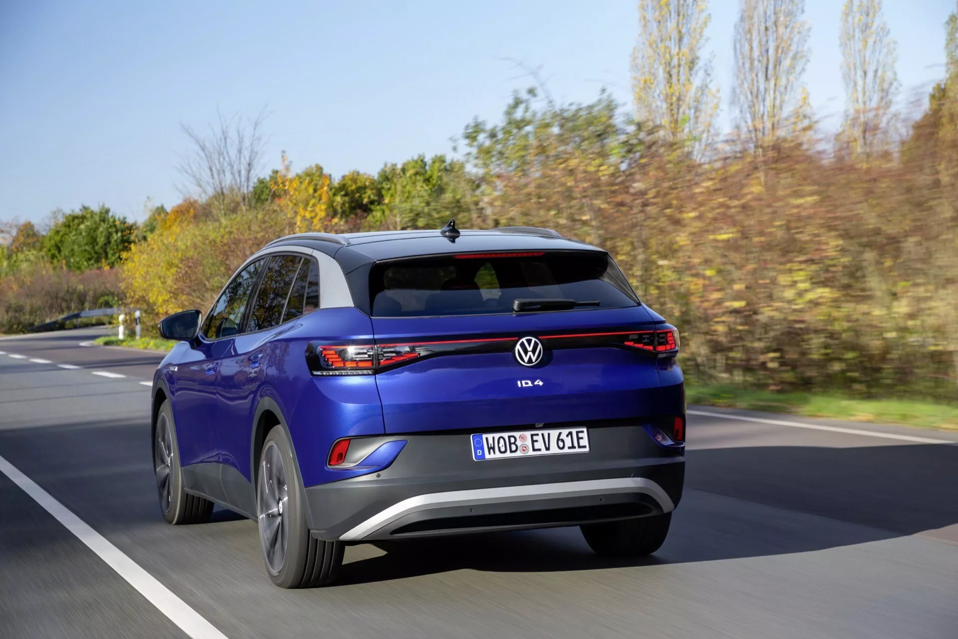Tylna perspektywa niebieskiego elektrycznego SUV-a Volkswagen ID.4 w ruchu na rozmytym tle drogi, podkreślając charakterystyczne tylne światła, zderzak tylny, klapę bagażnika z emblematem VW i dynamiczną postawę