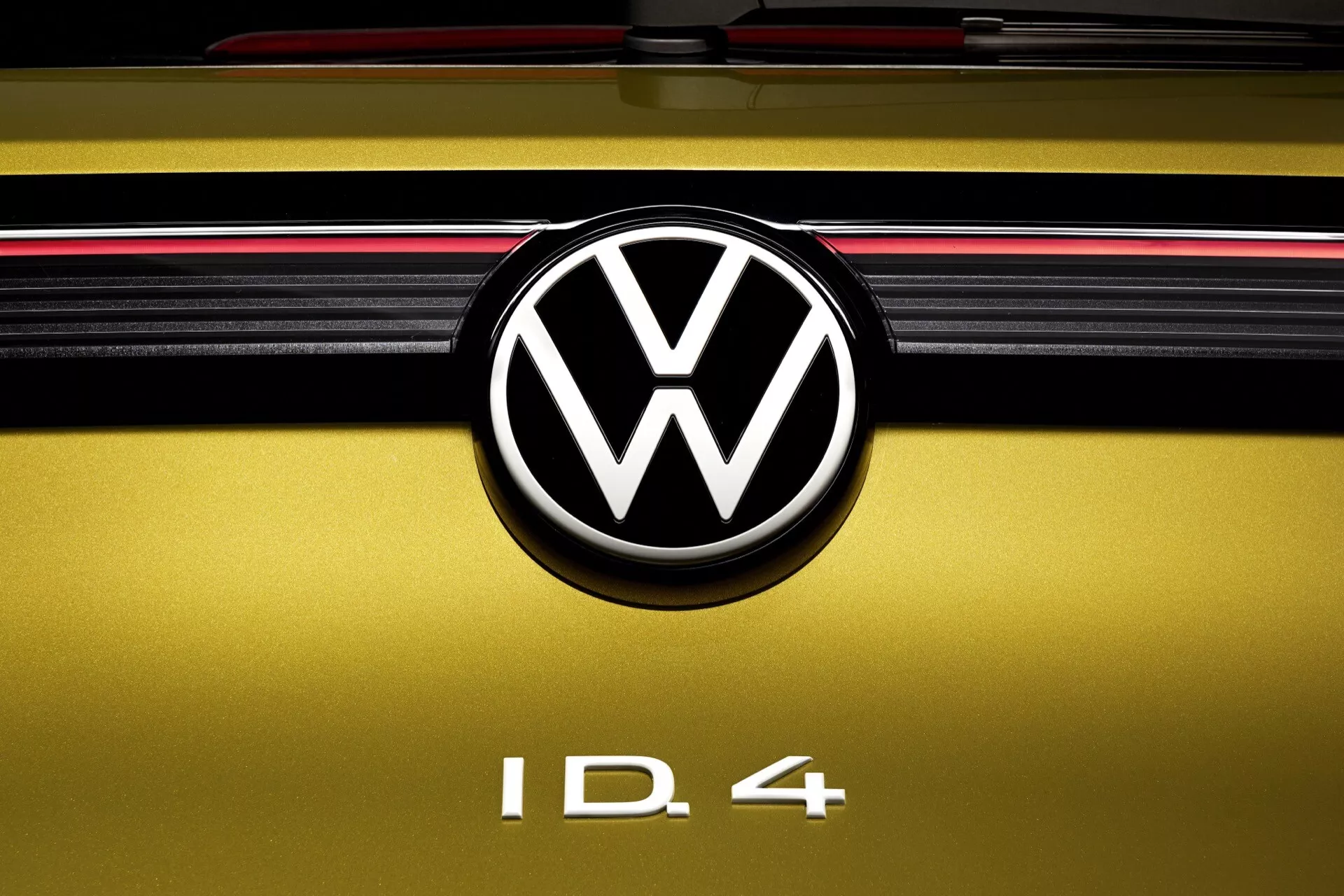 Zbliżenie na tylną klapę Volkswagena ID.4 2020 z wyeksponowanym emblematem VW, oznaczeniem modelu i elementami designu w tym złotożółtym kolorem i czerwonym paskiem światła zadnego