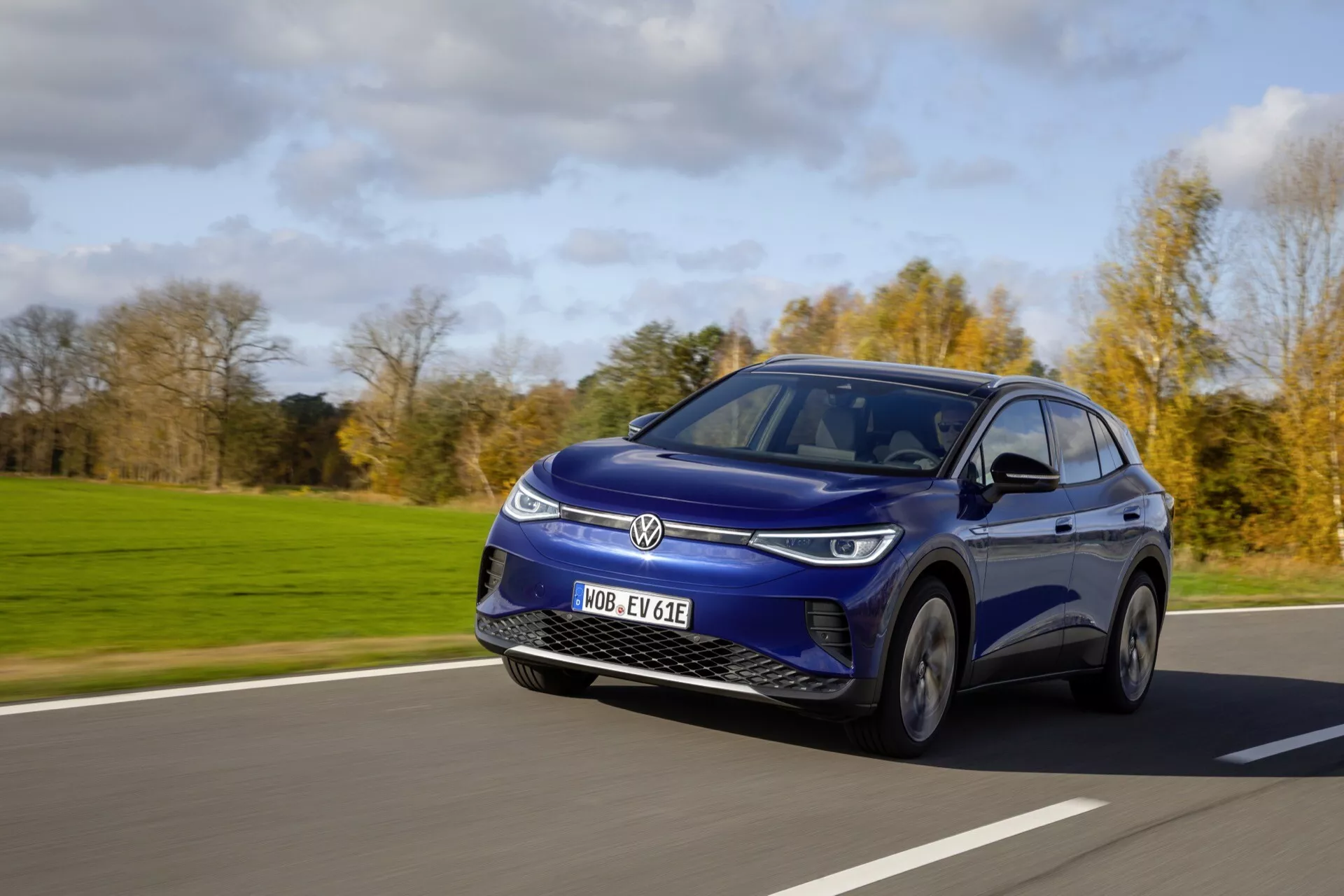 Dynamiczny obraz niebieskiego elektrycznego SUV-a Volkswagen ID.4 z 2020 roku w ruchu pod bezchmurnym niebem, prezentujący jego elegancki design, światła LED i cechy aerodynamiczne z niskiej perspektywy, z widoku trzech czwartych od frontu lewej strony.