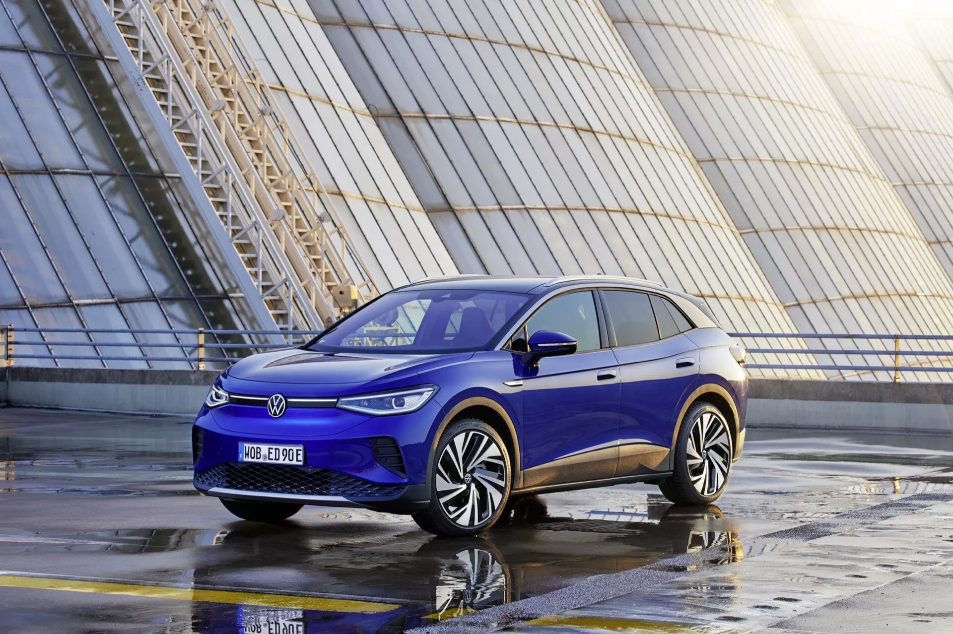 Elektryczne SUV VW ID.4 1. generacji z 2020 roku w kolorze niebieskim, widziane z niskiego przedniego kąta trzech czwartych podkreślające jego diody LED, zamkniętą przednią kratkę, aerodynamiczny zderzak i nowoczesny design kół w miejskim otoczeniu