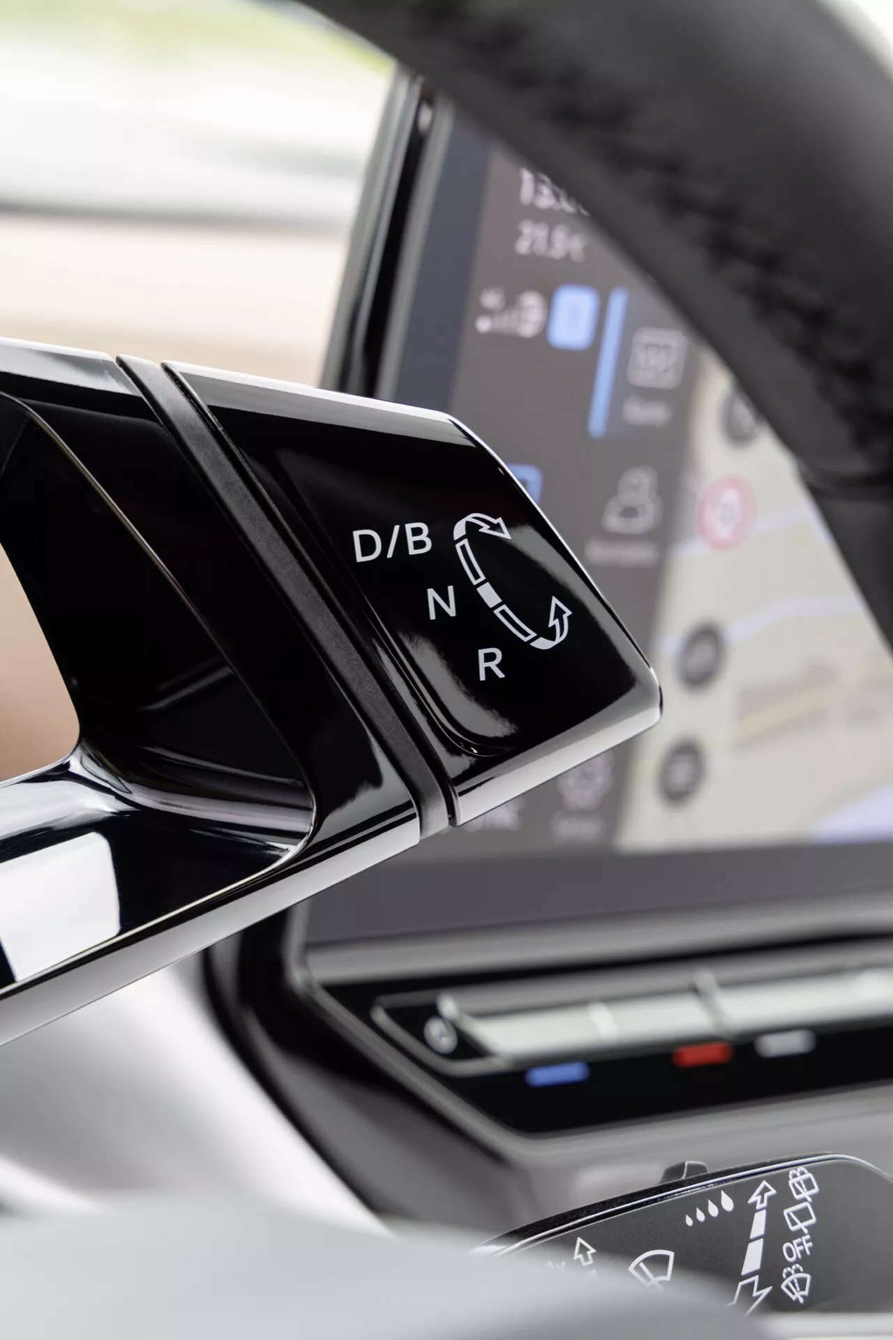 Zbliżenie na wnętrze VW ID.4 2020, pokazujące nowoczesny dźwignię zmiany biegów z połyskliwym czarnym wykończeniem i białymi literami Drive, Brake/Battery, Neutral, Reverse oraz dotykowy panel kontrolny w tle