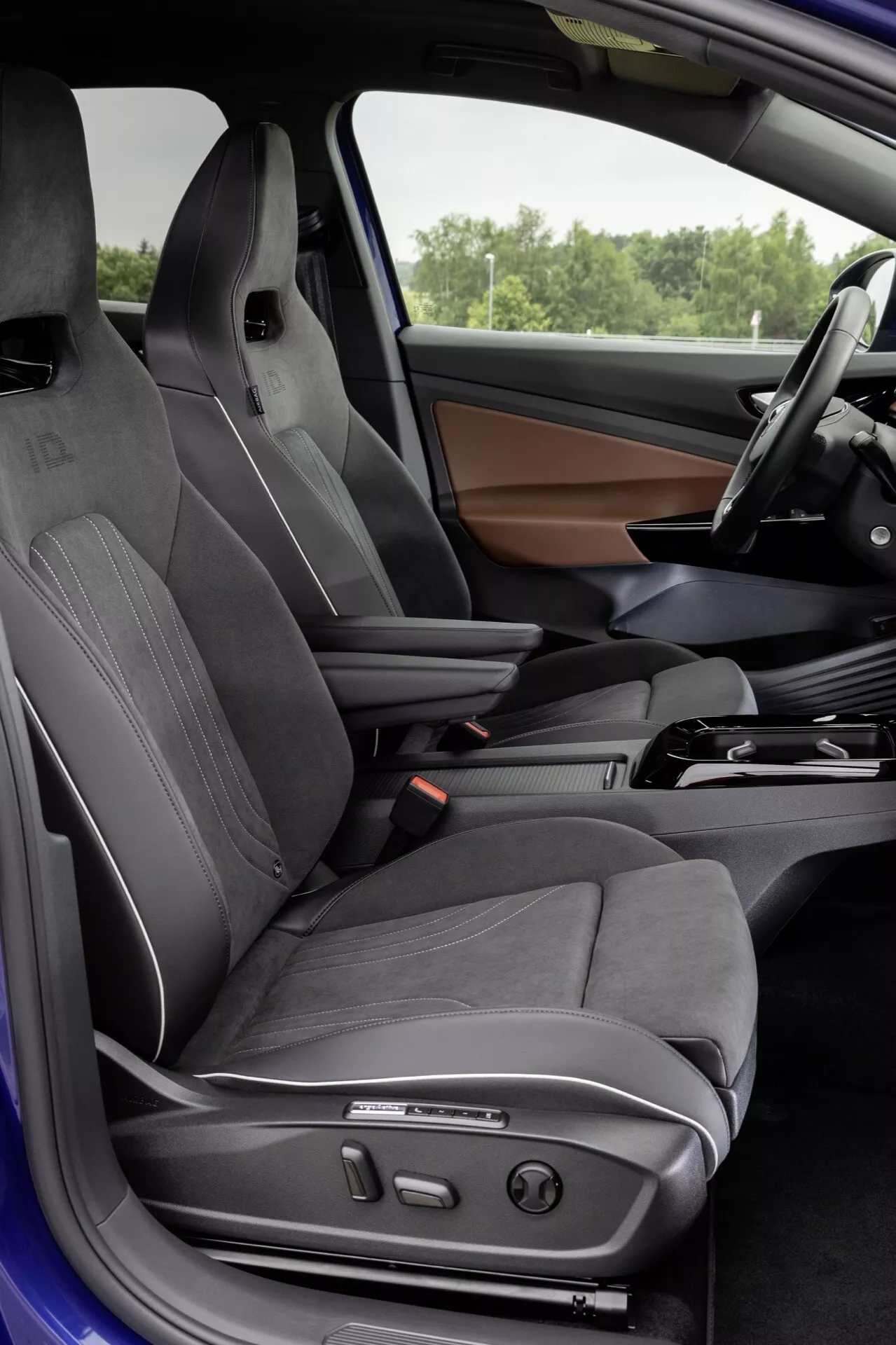 Widok wnętrza VW ID.4 1. generacji z 2020 roku z perspektywy otwartych drzwi kierowcy, pokazujący sportowe fotele kubełkowe, zaawansowane funkcje sterowania i elegancką deskę rozdzielczą