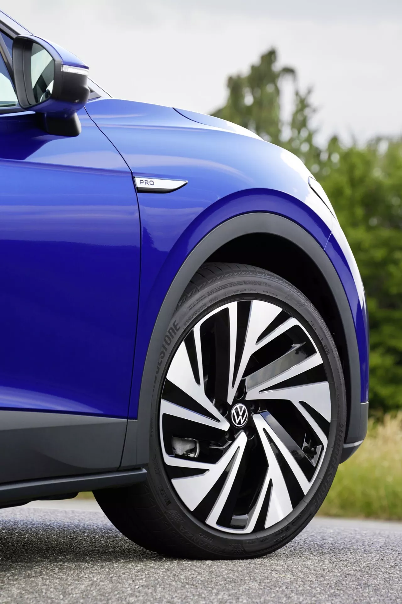 Zbliżenie na bok niebieskiego VW ID.4 z 2020 roku, pokazujące przednie koło z nowoczesnym designem alufelgi, oponę Bridgestone i emblemat eHybrid, co podkreśla sportowy wygląd i technologię hybrydową.