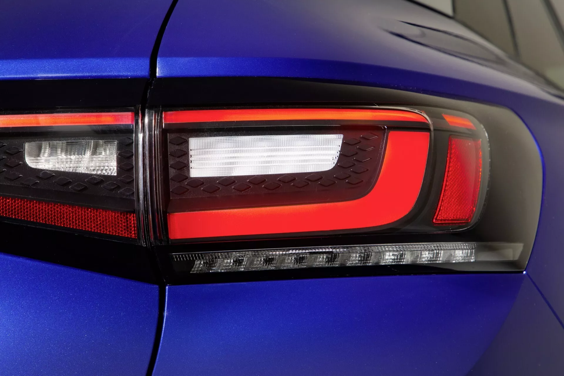 Zbliżenie na tylną lampę po prawej stronie niebieskiego VW ID.4 2020 prezentujące nowoczesną technologię LED, w tym sekcje świateł hamowania, kierunkowskazów, cofania i możliwie światła przeciwmgielnego z żywymi czerwonymi i przezroczystymi sekcjami na błyszczącym nadwoziu.