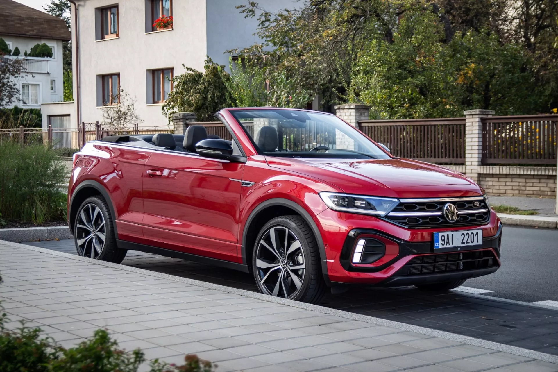Czerwony kabriolet VW T-Roc 2022, prezentujący dynamiczny design z długą, opadającą ku przodowi maską, nowoczesną przednią kratą, smukłymi reflektorami i aerodynamicznym profilem, uchwyconym z perspektywy trzech czwartych z przodu na ulicy