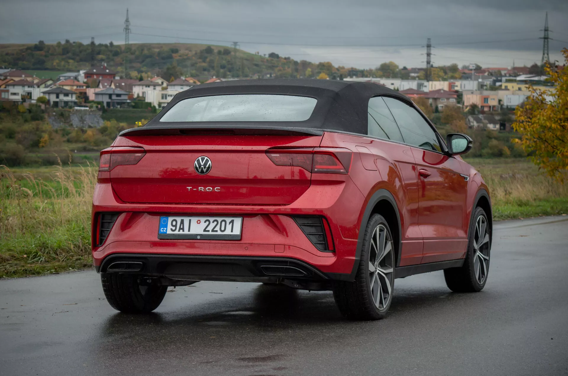 Czerwony Volkswagen T-Roc Cabriolet 2022 w widoku z tylnej części trzy czwarte na mokrej drodze, prezentujący tylny design, profil boczny, design kół, tylnie światła LED, tylny zderzak z wbudowanymi czujnikami, podwójne rury wydechowe, wieloramienne felgi aluminiowe, i składany dach