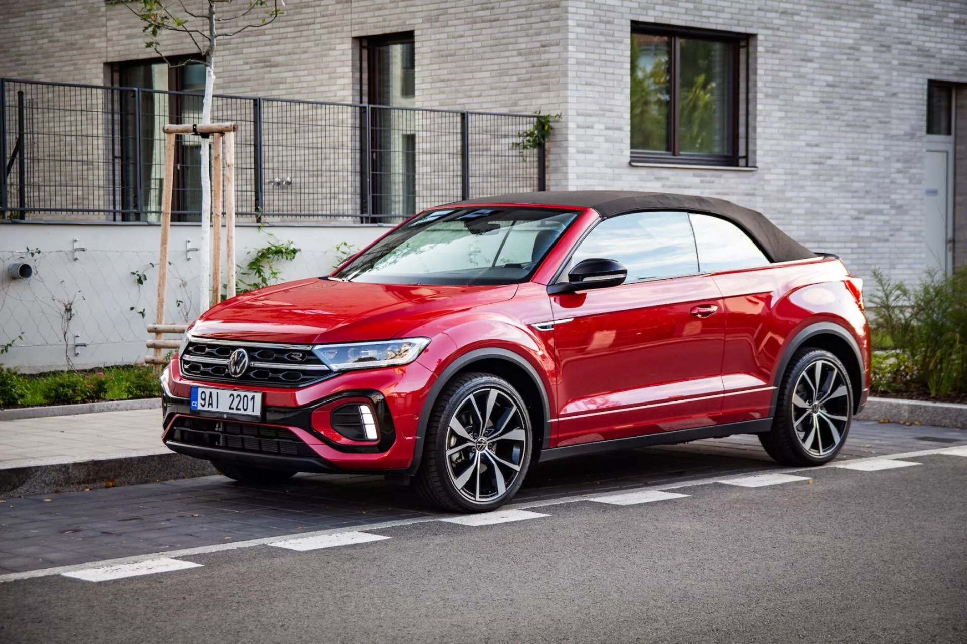 Jaskrawoczerwony kabriolet crossover SUV VW T-Roc 2022 zaparkowany przy ulicy, prezentujący grill przedni, reflektory LED, felgi aluminiowe i miękki dach, w trzy-czwartym widoku z przodu przy jasnej pogodzie