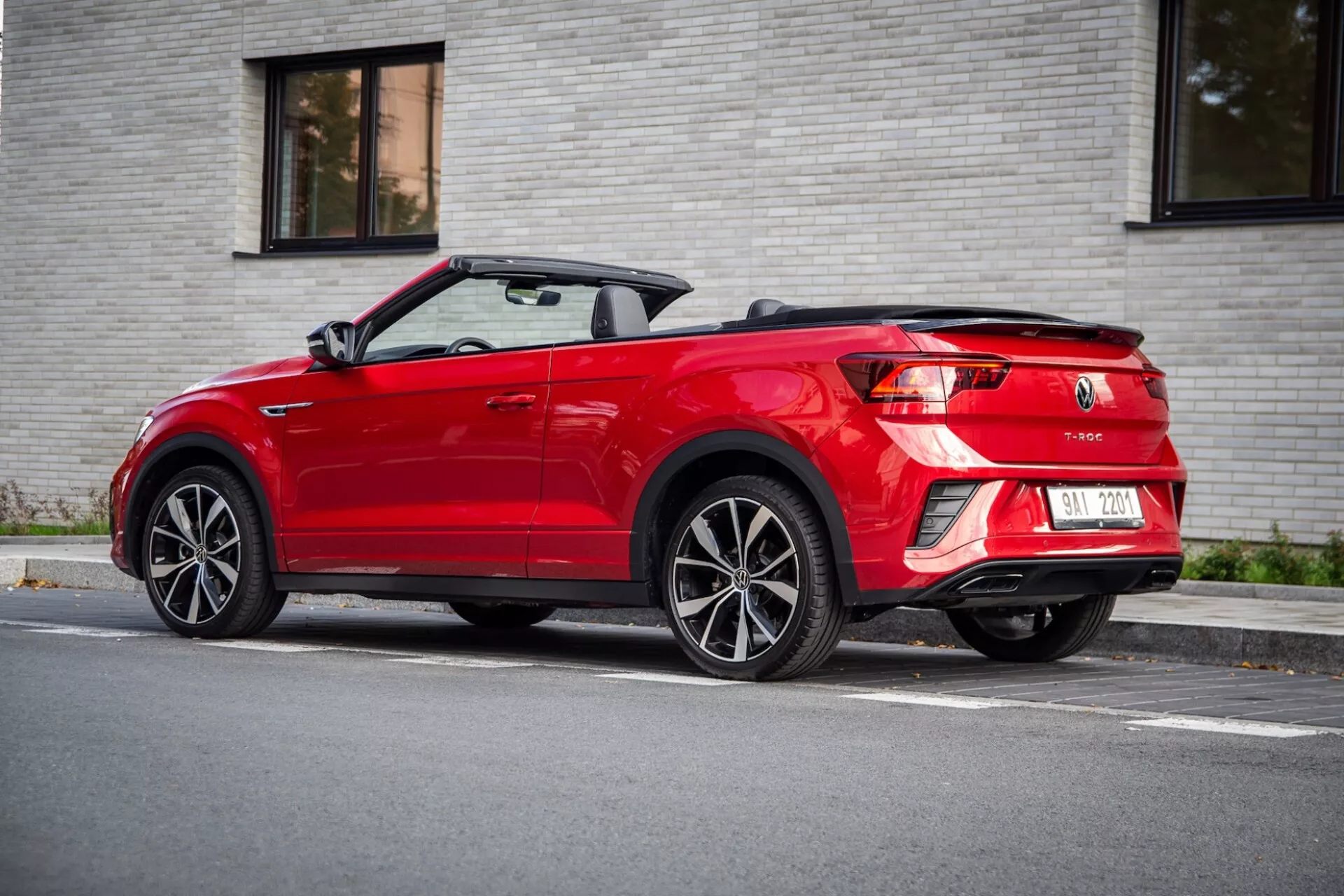 Widok z tyłu o trzech czwartych czerwonego VW T-Roc Cabriolet z 2022 roku z opuszczonym miękkim dachem, pokazujący diody LED tylne światła, podwójny wydech i wieloramienne koła ze stopów lekkich, zaparkowany na ulicy w miękkim świetle dziennym