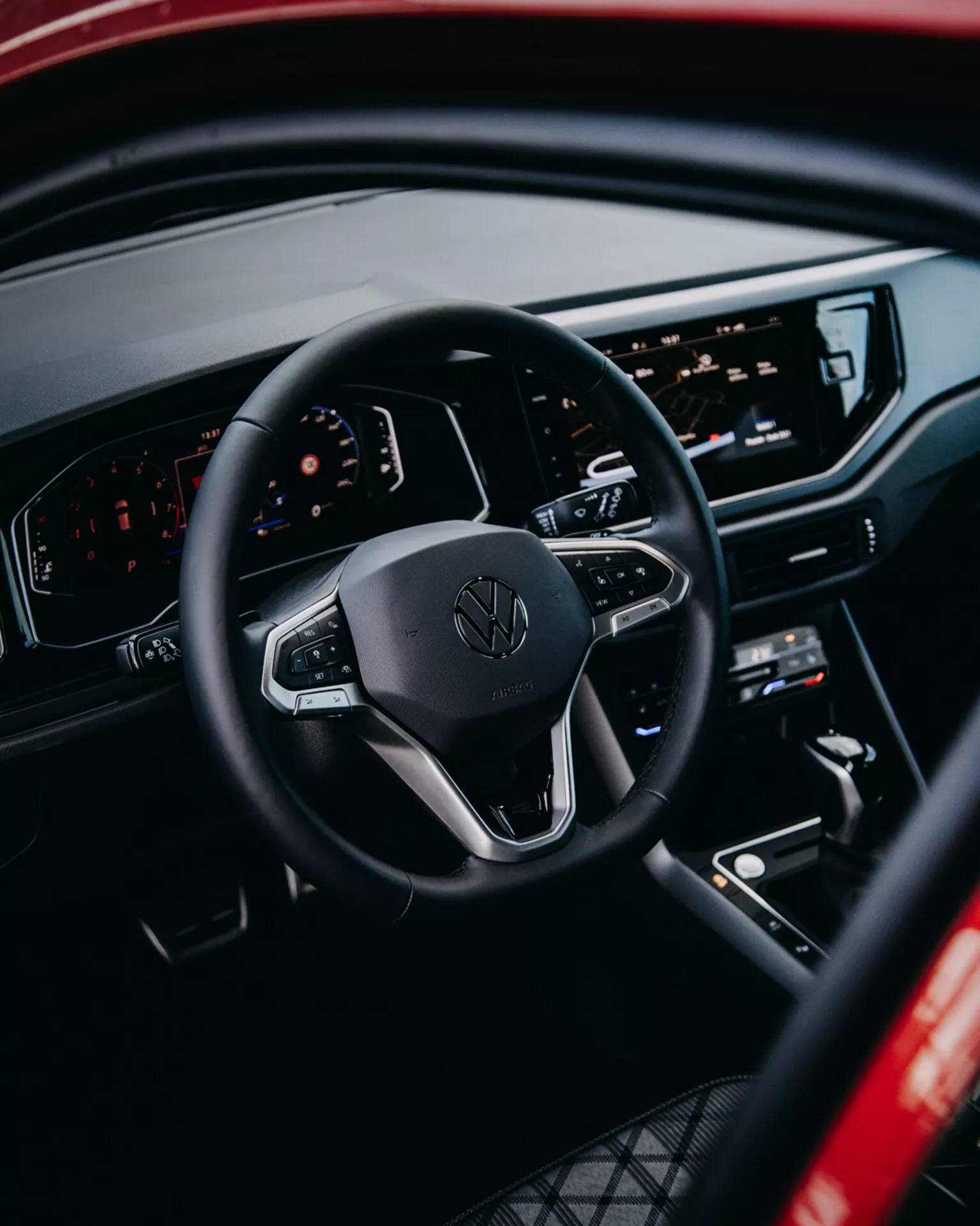 Widok wnętrza Volkswagen Taigo 2021 z akcentem na kierownicę z kontrolami, cyfrowy deska rozdzielcza i centralna konsola infotainment z perspektywy tylnego pasażera