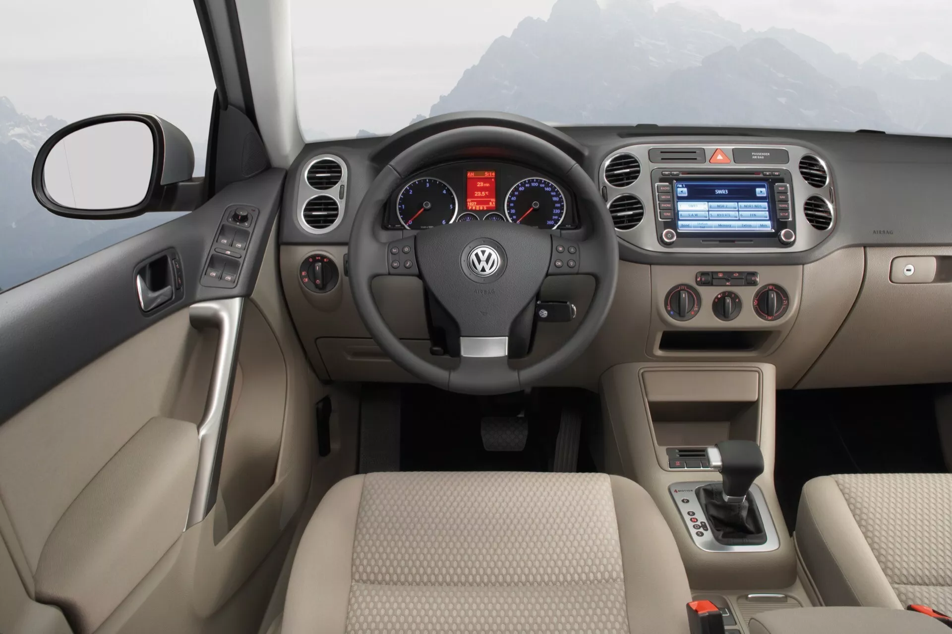Wnętrze Volkswagen Tiguan 2007 z dwukolorową deską rozdzielczą, wielofunkcyjną kierownicą, analogowym zestawem wskaźników, systemem multimedialnym z kolorowym ekranem, manualną kontrolą klimatyzacji i automatyczną dźwignią zmiany biegów.