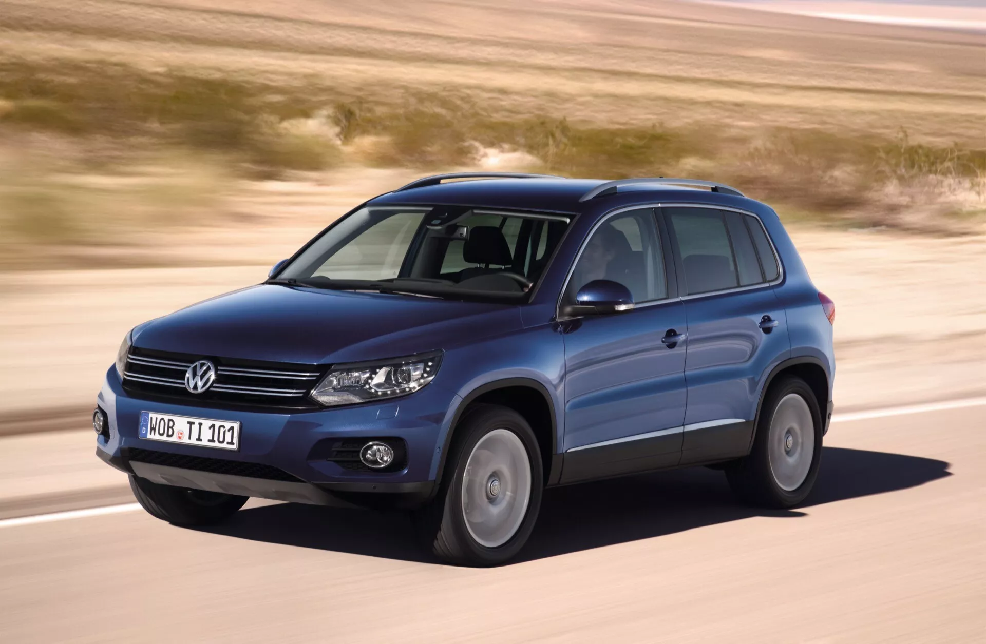 Volkswagen Tiguan z 2007 roku w ruchu, uchwycony z kąta przedniego trzy czwarte z widokiem na stronę kierowcy, wyposażony w alufelgi, relingi dachowe, świecące reflektory, na tle płaskiego, jałowego terenu