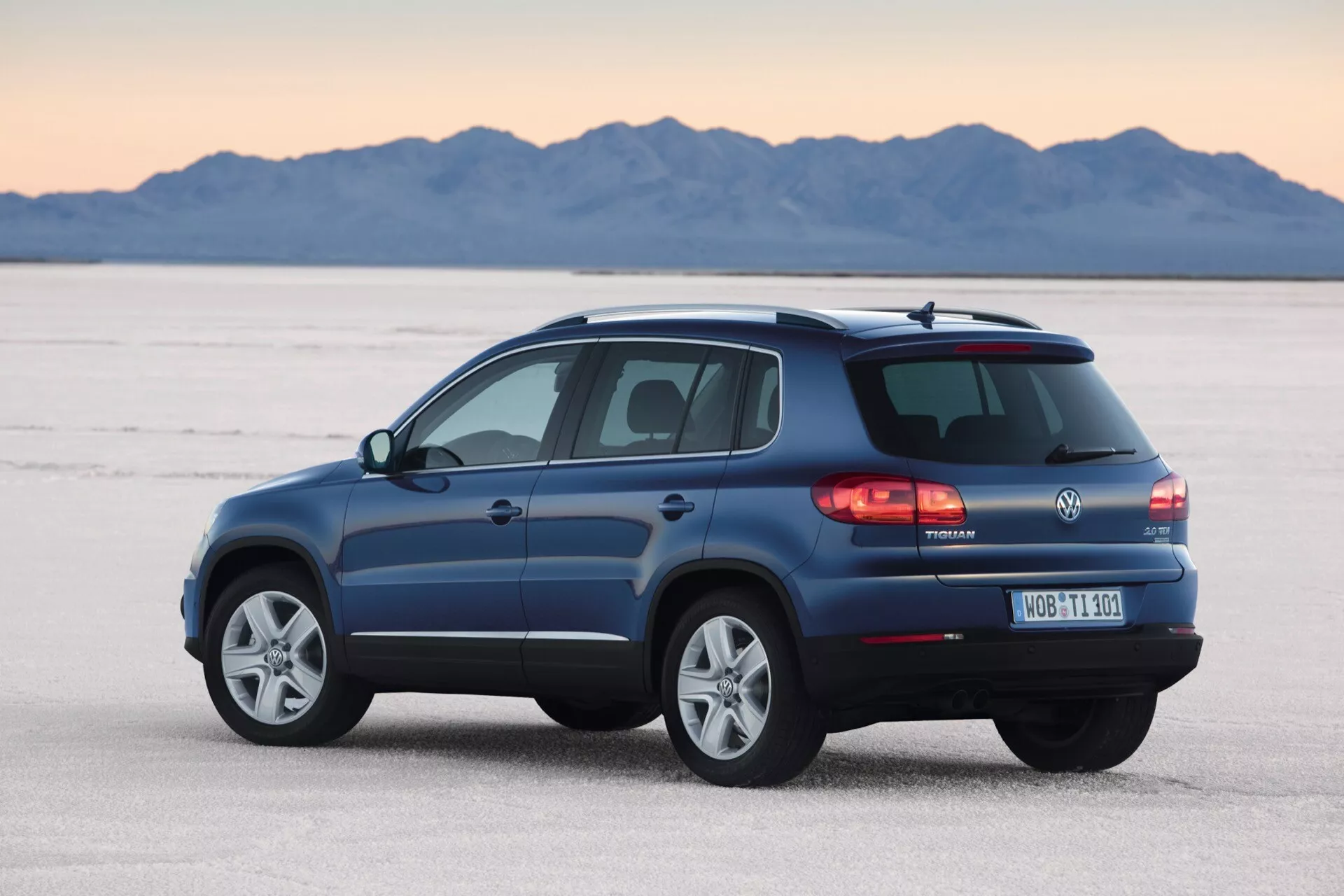 Volkswagen Tiguan 2007 w kolorze metalicznym niebieskim, prezentujący swój design i cechy z perspektywy trzy czwarte tylnej części na płaskiej solnisku, z wyeksponowanymi detalami takimi jak tylne światła LED, tylna wycieraczka, relingi dachowe, koła ze stopów lekkich i rura wydechowa