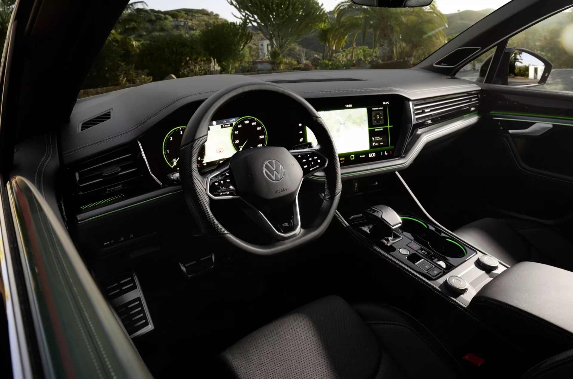 Widok wnętrza Volkswagen Touareg 2023 z tylnej kanapy, prezentujący deskę rozdzielczą, cyfrowe wyświetlacze, kierownicę z zamontowanymi sterowaniami i konsolę środkową w modernistycznym i luksusowym wyglądzie