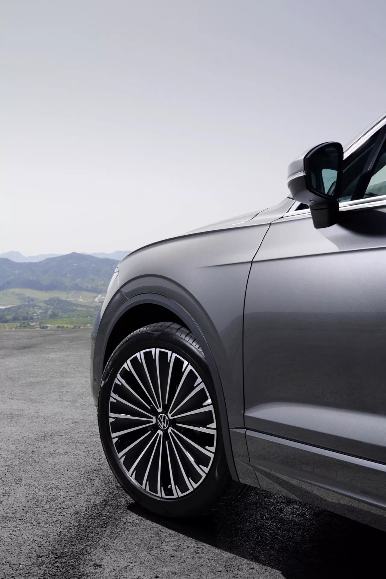 Zbliżenie na przedni panel boczny kierowcy Volkswagen Touareg 2023 (III Facelift) pokazujący duże, stylowe koło ze stopu z złożonym wieloszprychowym wzorem, odzwierciedlające jakość pojazdu premium na tle górzystego krajobrazu.