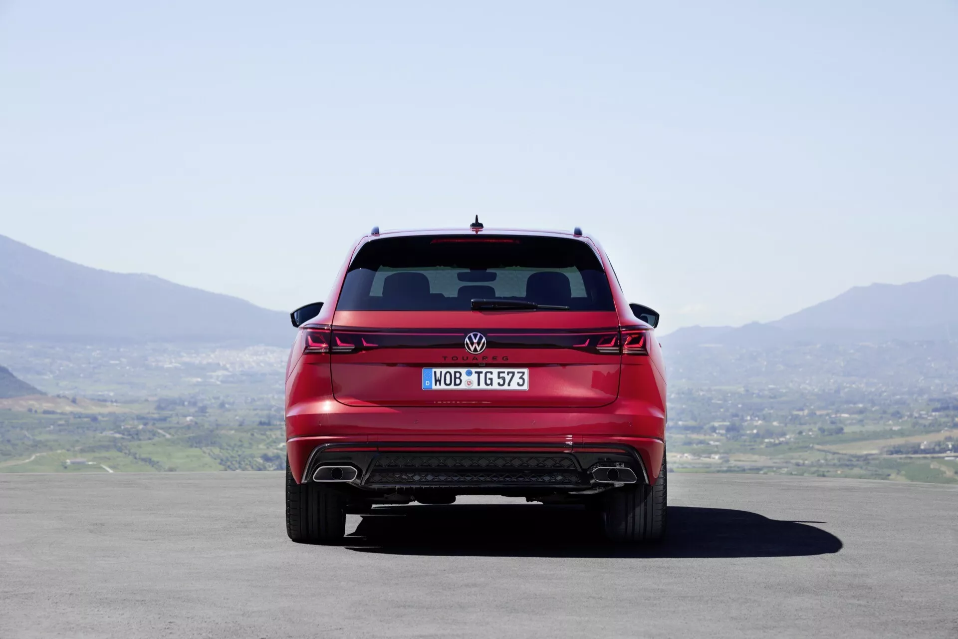 Tylny widok Volkswagen Touareg 2023 prezentujący pełną szerokość, nowoczesne tylne światła, dyfuzor tylny oraz podwójne końcówki wydechu, w naturalnym świetle dziennym z jasnym niebem i pagórkowatym krajobrazem w tle