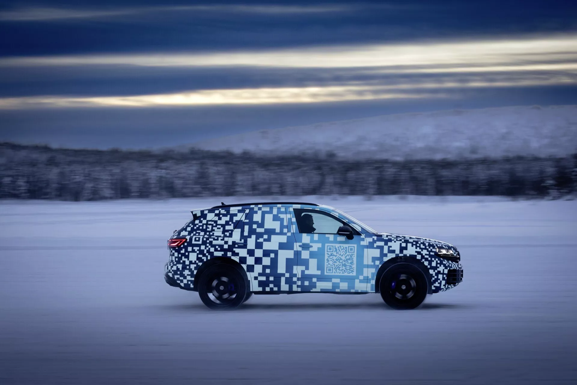 VW Touareg 2023 (III-lifting) w ruchu, podkreślający aerodynamiczny design i tylne światła LED, z kamuflażem, w zimowej scenerii testowej