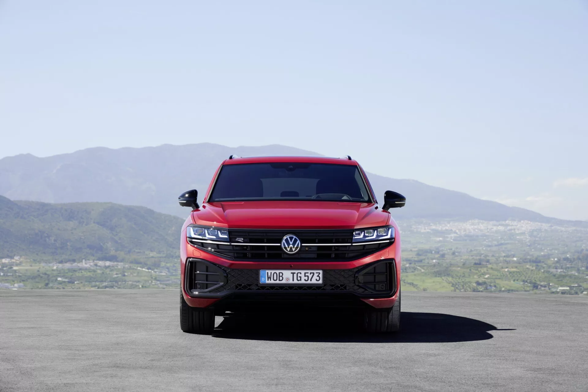 Widok z przodu czerwonego Volkswagena Touareg III facelift 2023, pokazujący zintegrowany grill i zespoły świateł LED, podkreślający dominację i nowoczesne cechy technologiczne pojazdu