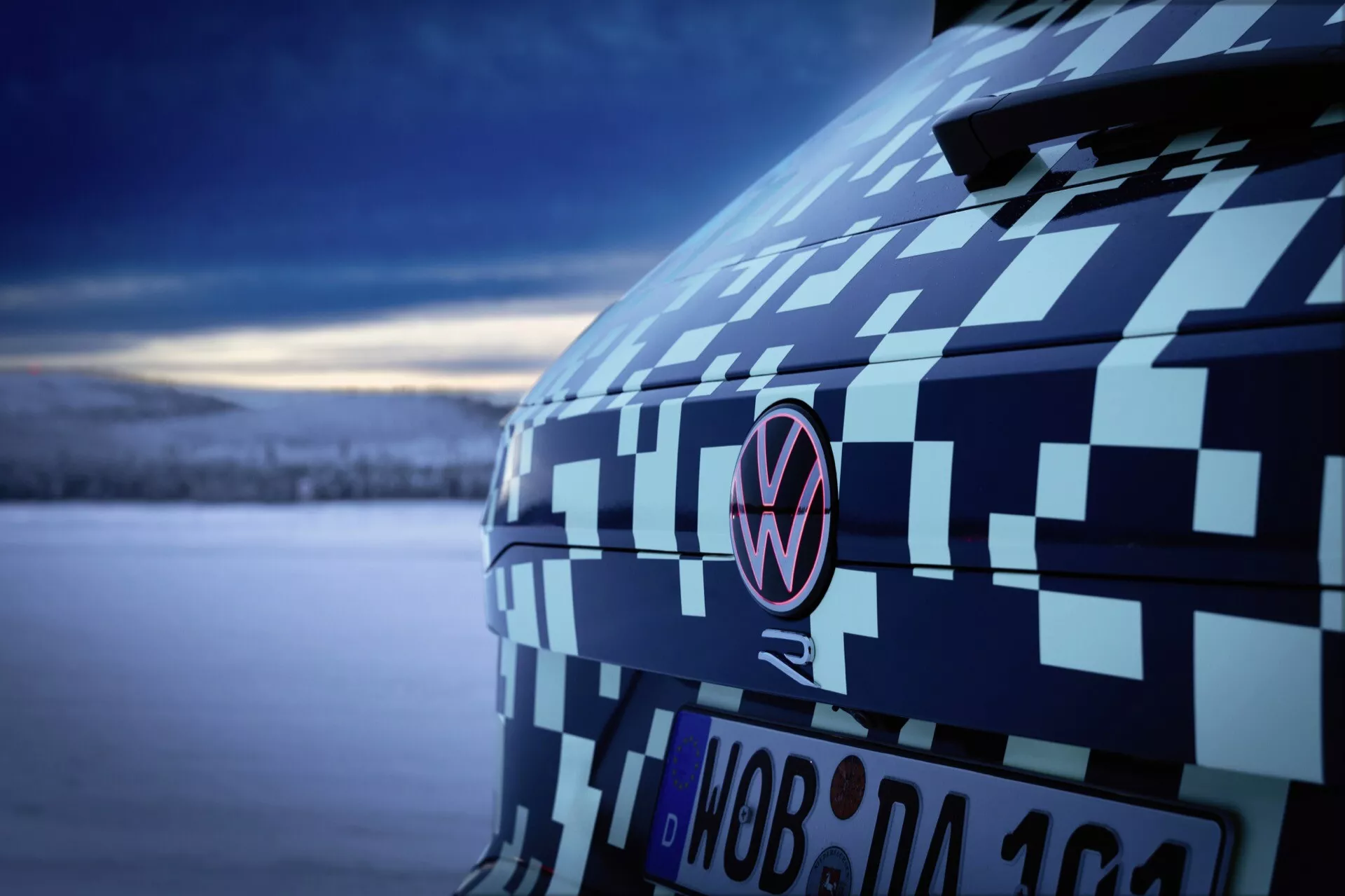 Zbliżenie na tylną część Volkswagena Touarega (III Facelift) rok 2023 w kamuflażu podkreślającym słup C i emblemat o zmierzchu, prezentujące testowanie prototypów samochodów i design pod miękkim, chłodnym oświetleniem