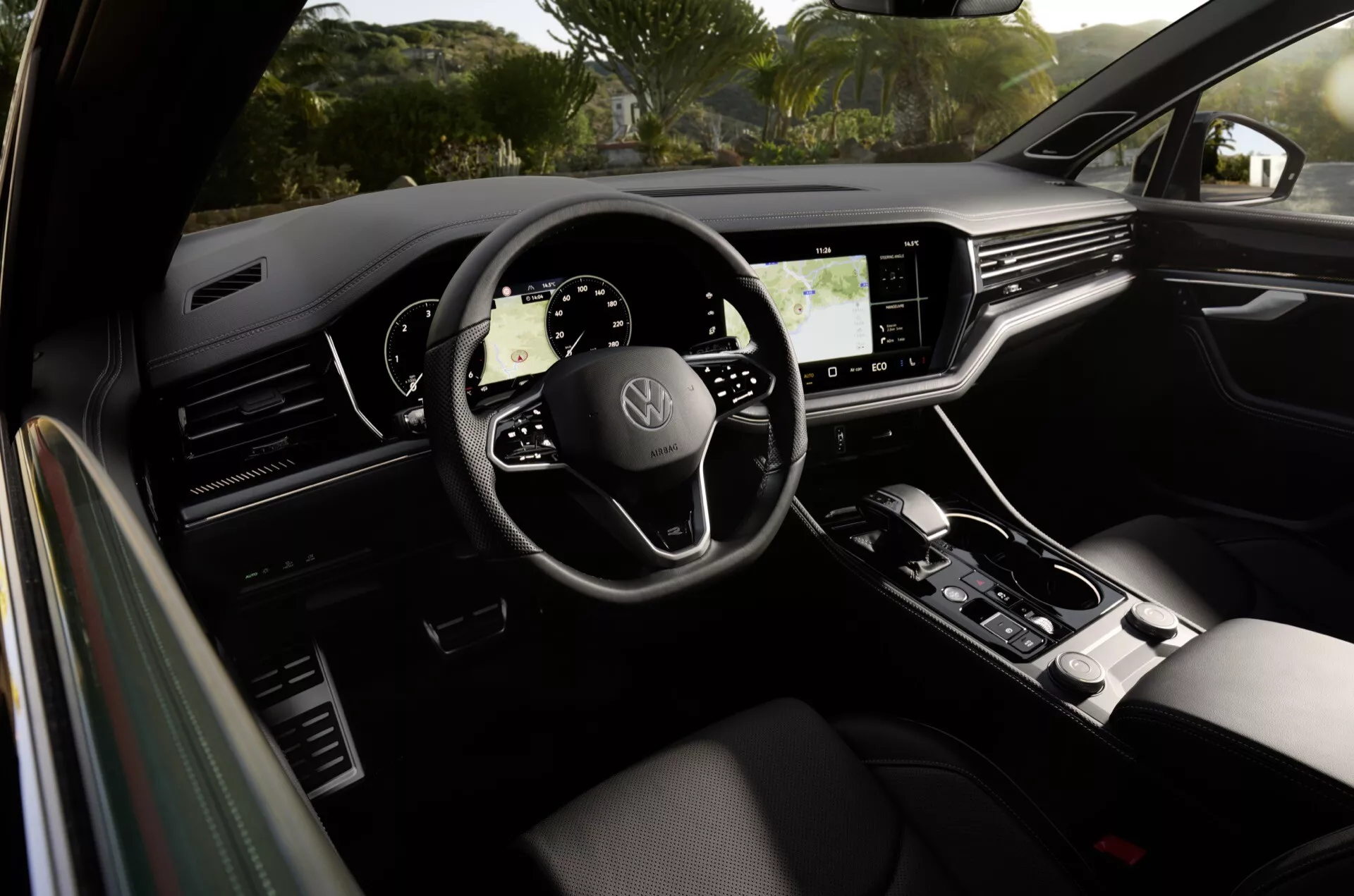 Wnętrze Volkswagen Touareg 2023 prezentujące kierownicę trójramienną z logo marki, w pełni cyfrowy panel wskaźników, duży ekran dotykowy systemu infotainment i elegancką dźwignię zmiany biegów, podkreślające nowoczesny design samochodu i zaawansowane funkcje technologiczne