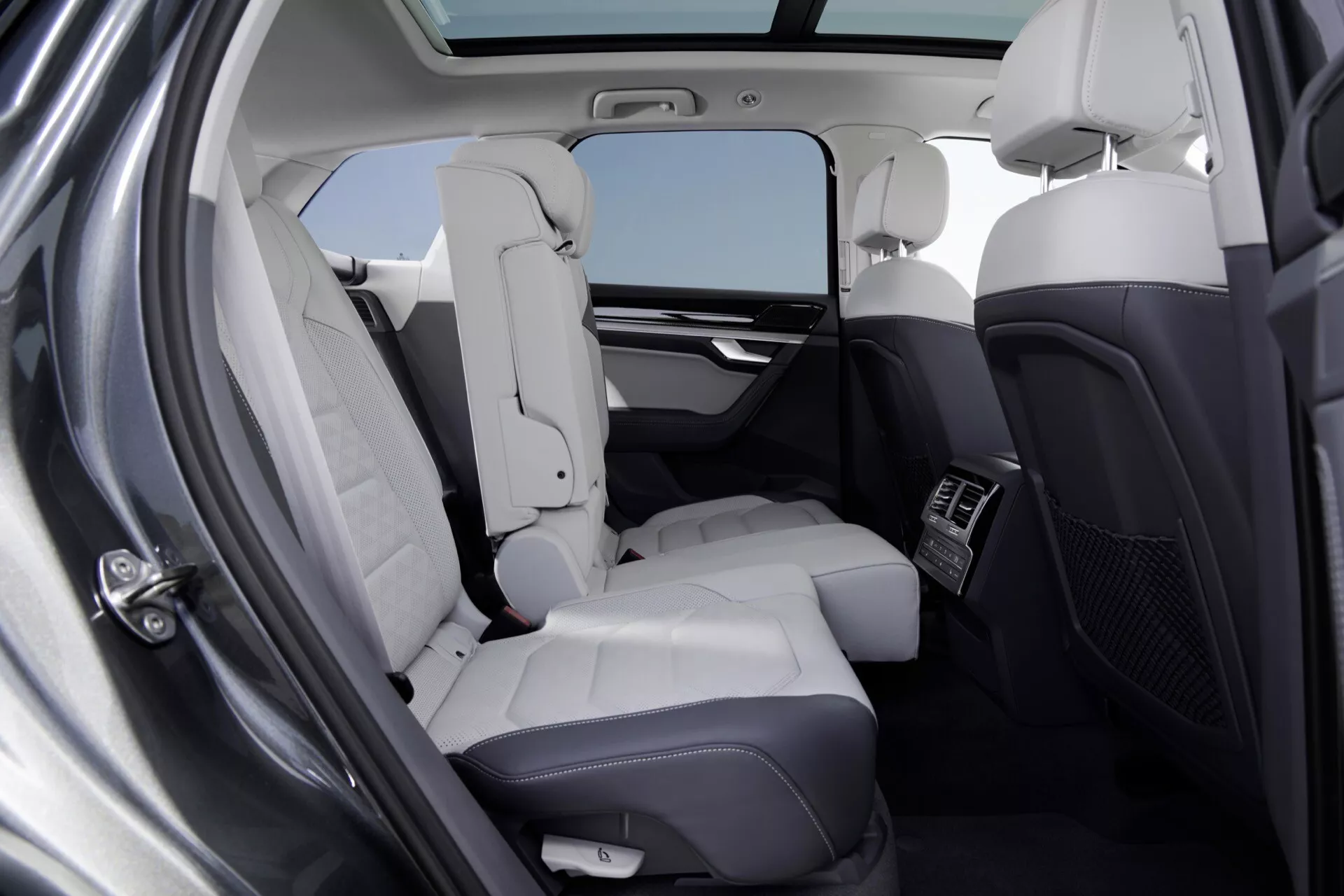 Wnętrze Volkswagen Touareg 2023 (III-Facelift) przedstawiające luksusową tylną część pasażerską z jasnymi skórzanymi siedzeniami, panoramicznym dachem i przestronną przestrzenią na nogi