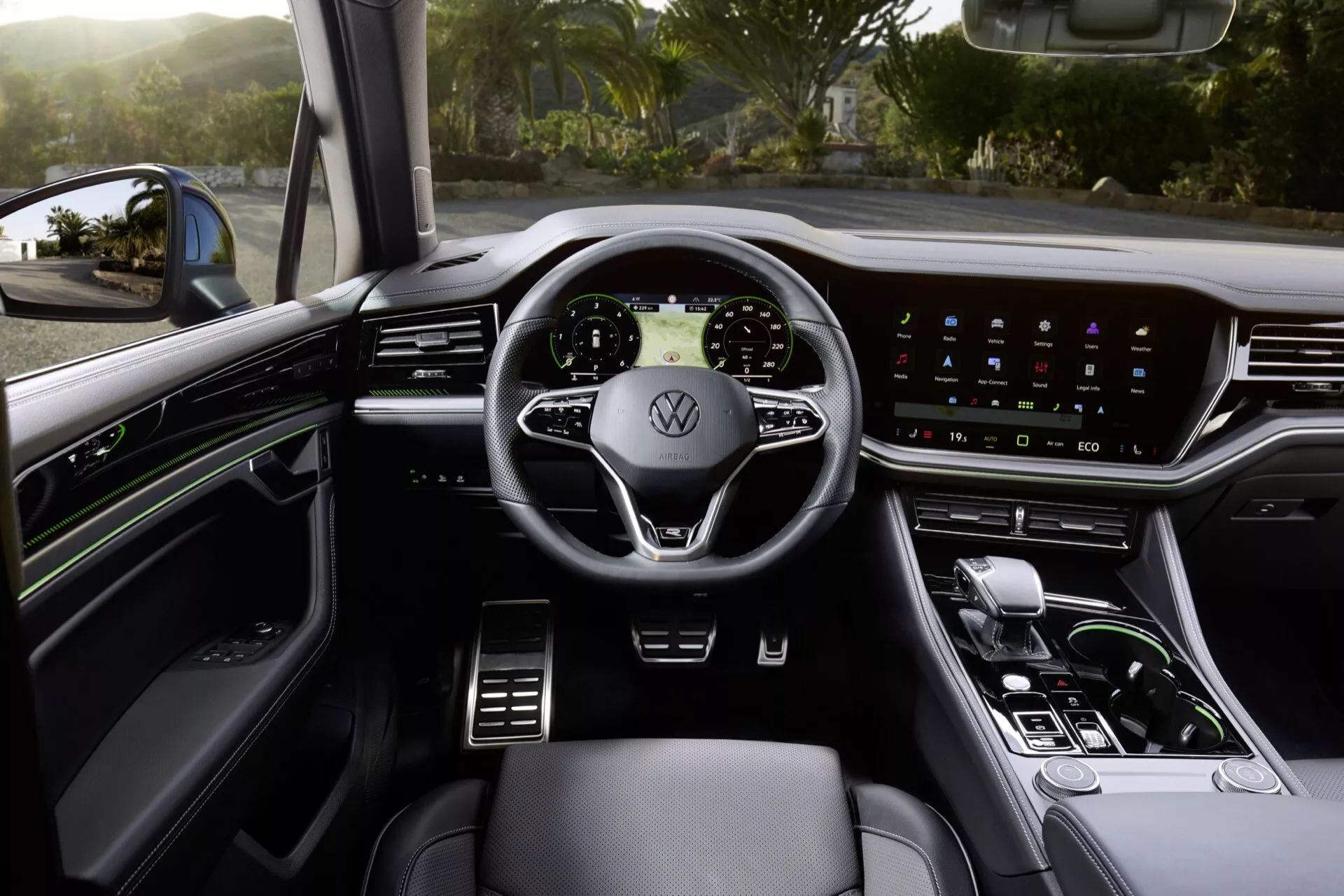 Widok wnętrza Volkswagen Touareg 2023 z perspektywy fotela kierowcy, pokazujący kierownicę z wbudowanymi kontrolkami, cyfrowy panel przyrządów, system infotainment z ekranem dotykowym, elegancką dźwignię zmiany biegów i tapicerkę premium z oświetleniem ambientowym