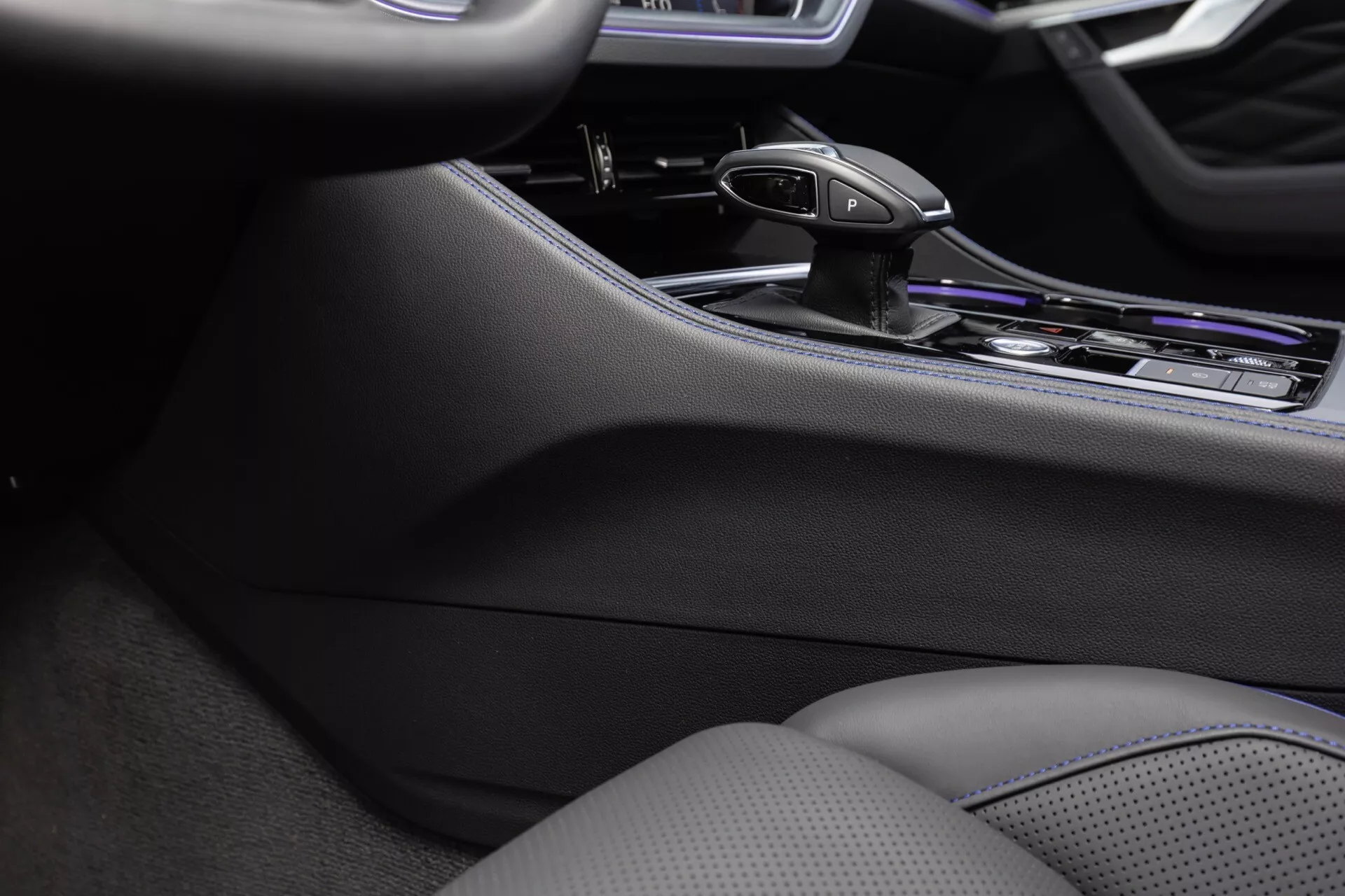 Szczegół wnętrza Volkswagen Touareg 2023 z konsolą środkową, ergonomiczną dźwignią zmiany biegów automatycznej skrzyni biegów i premium wykończeniami chromowymi, podkreślający zaawansowane sterowanie systemem infotainment i siedzenia z kontrolą klimatu