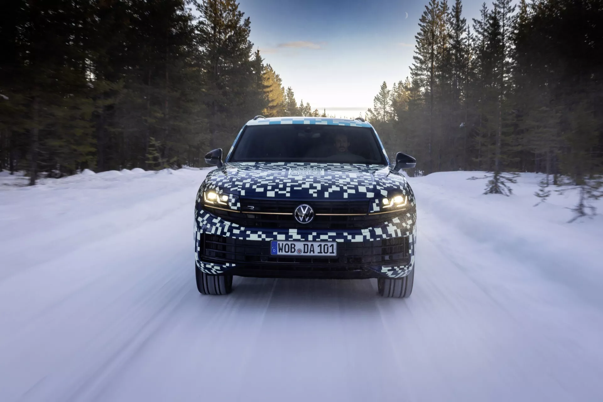 Przód VW Touareg 2023 (III-Facelift) na drodze pokrytej śniegiem, przedstawiający reflektory LED, szeroką atrapę i kamuflowaną tablicę rejestracyjną, odzwierciedlający zaawansowane funkcje oświetleniowe i zimowe właściwości jezdne.