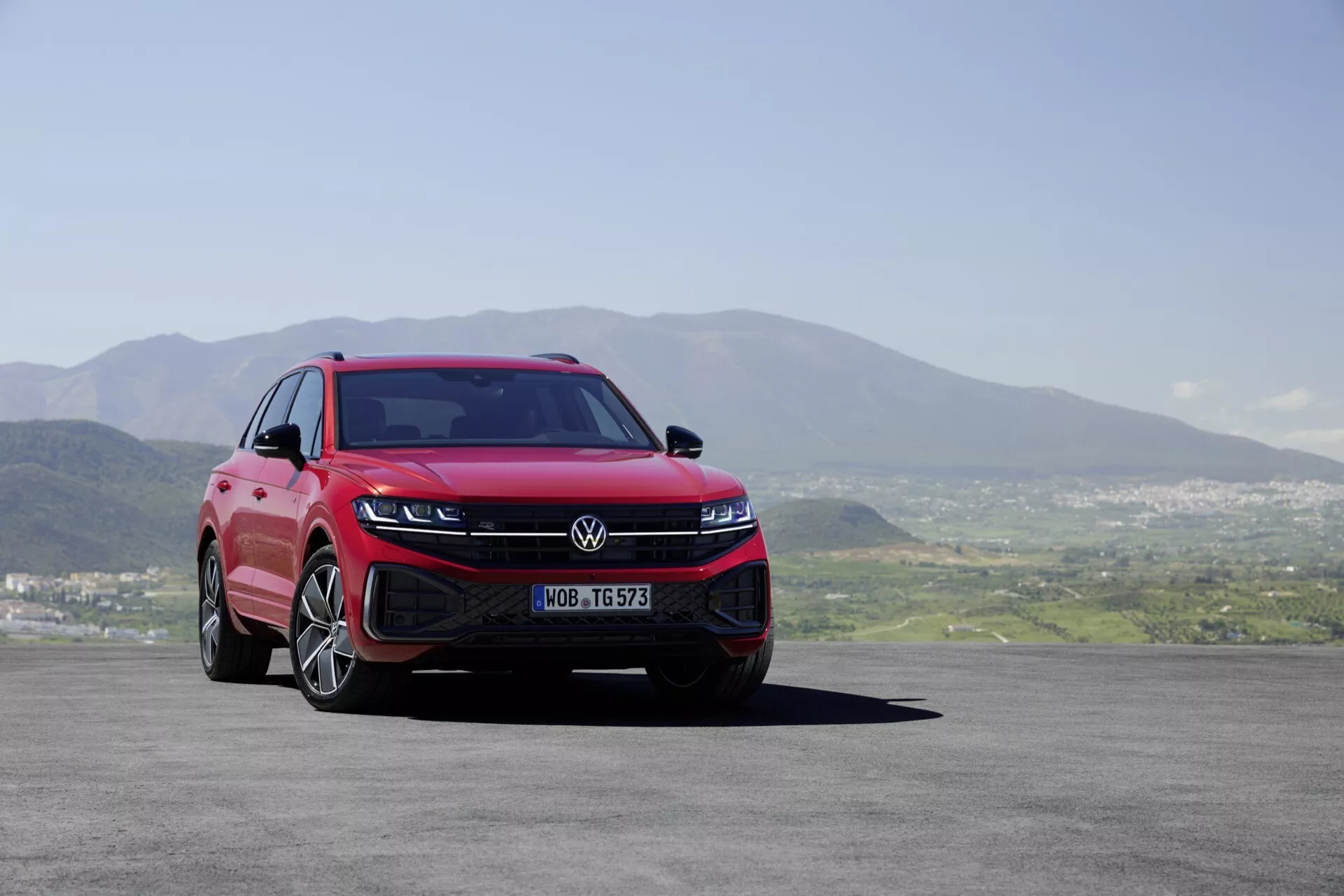 Volkswagen Touareg 2023 (III-Facelift) prezentuje swój nowoczesny wygląd z niskiej, przedniej perspektywy trzech czwartych, podkreślając reflektory LED, sportowy przedni zderzak, aerodynamiczną kratę i wieloramienne koła ze stopu lekkiego na tle malowniczego krajobrazu.