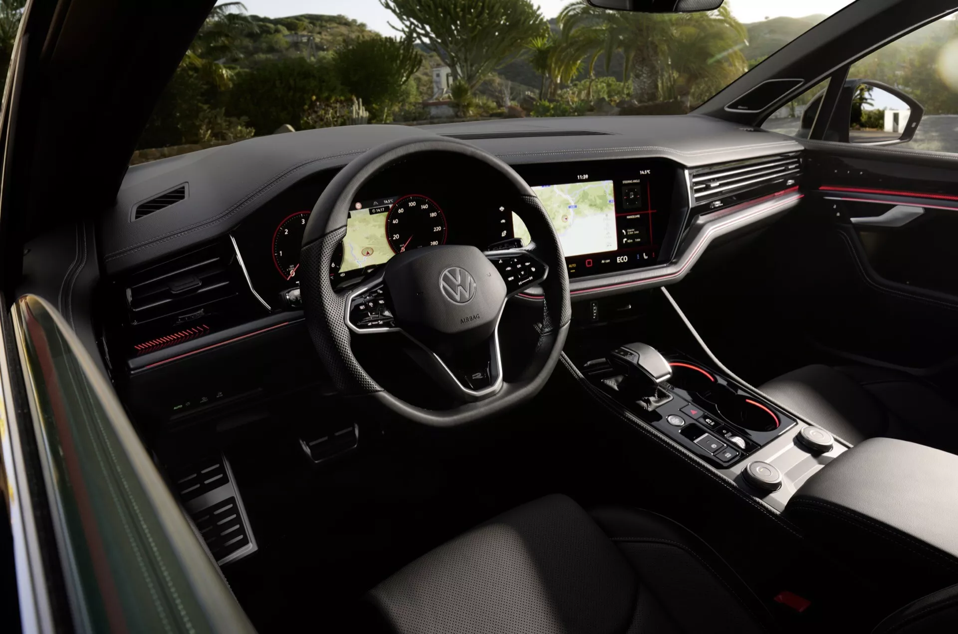 Widok wewnętrzny Volkswagen Touareg 2023 z tylnej kanapy pasażerskiej, pokazujący kierownicę z logo, cyfrowy zestaw wskaźników i dotykową konsolę centralną
