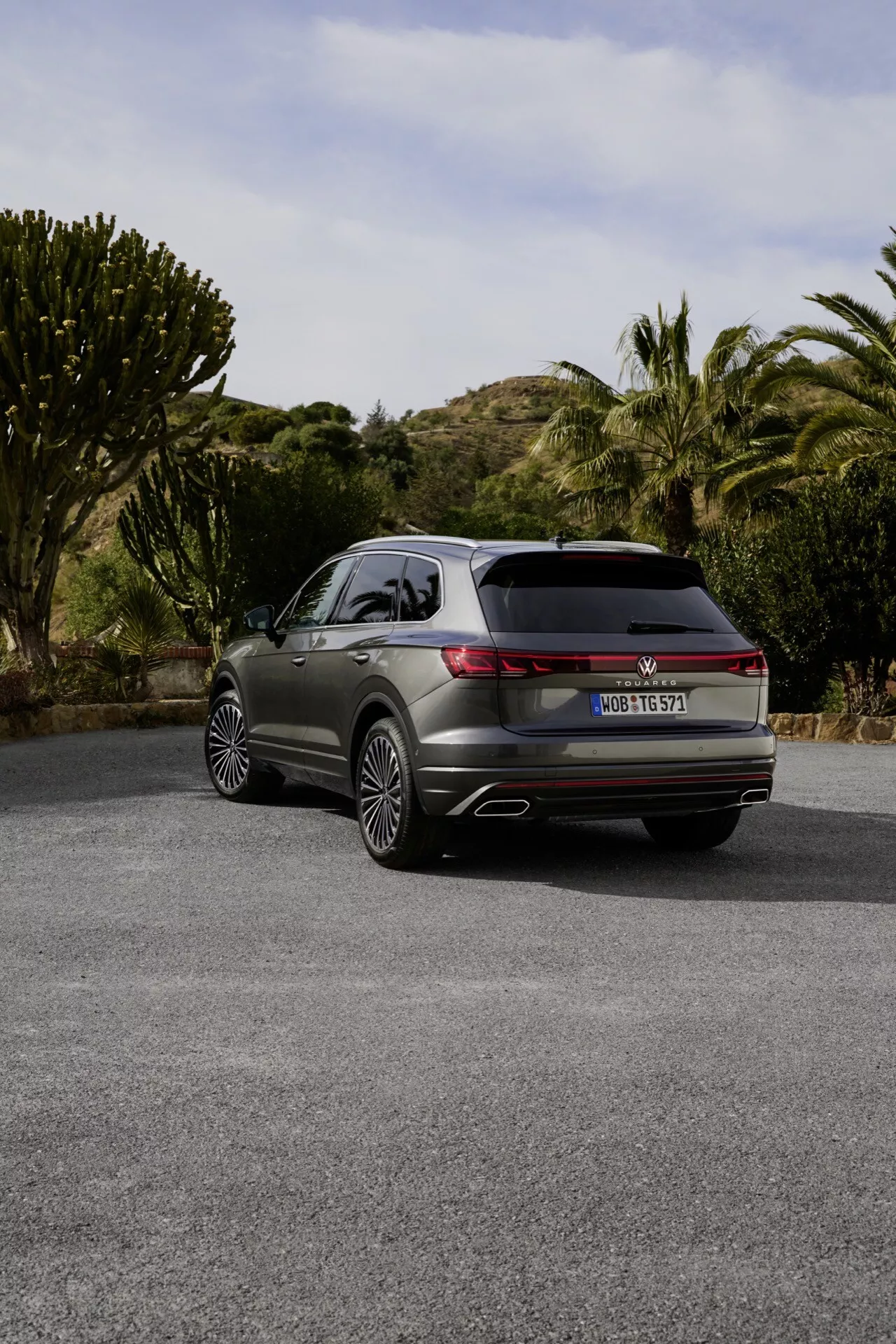 VW Touareg 2023 (III-facelift) pokazany z tylnej perspektywy trzech czwartych z LEDowymi światłami tylnymi, podwójnymi rurami wydechowymi i premium felgami aluminiowymi na półwiejskiej drodze