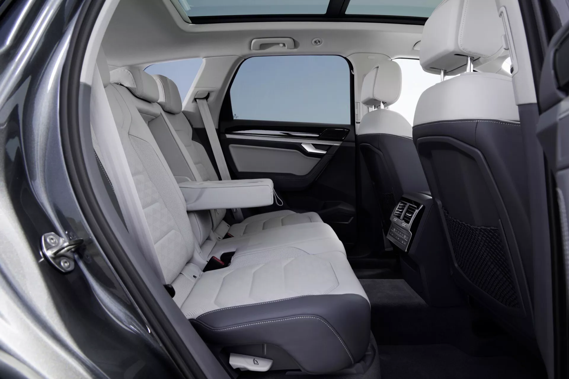 Wnętrze VW Touareg 2023 (III Facelift) prezentujące luksusowe tylne siedzenia z jasnej skóry pikowanej, zintegrowane funkcje technologiczne i oświetlenie z panoramicznego dachu
