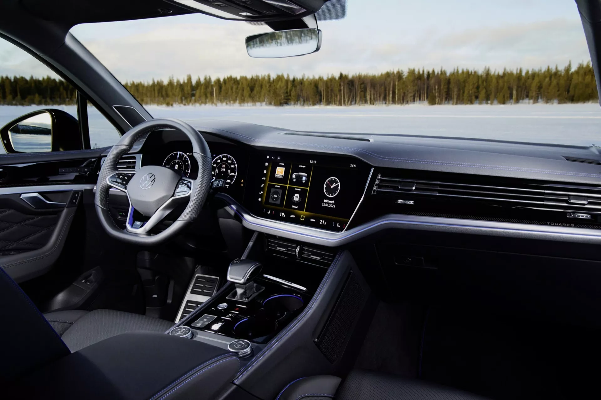 Widok wnętrza VW Touareg 2023 z perspektywy przedniego fotela pasażera: czarne skórzane siedzenie, konsola środkowa z dźwignią zmiany biegów, uchwyty na kubki, przyciski sterujące, ekran dotykowy systemu infotainment, klimatyzacyjne nawiewy, cyfrowy kokpit i kierownica z przyciskami sterującymi, na tle zimowego krajobrazu przez przednią szybę, podkreślające nowoczesne luksusowe funkcje i technologię pojazdu.
