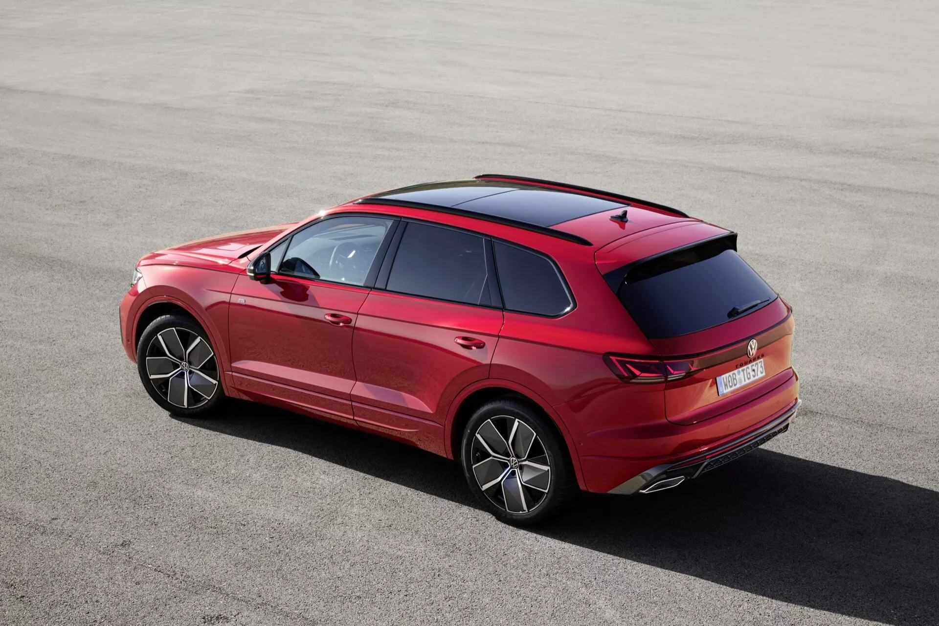 VW Touareg III po liftingu z 2023 roku widziany z wysokiego tylnego kąta trzech czwartych ukazujący jego elegancką sylwetkę, charakterystyczne linie nadwozia, linię dachu, szczegółowe wzornictwo tylnego spoilera i anten, innowacyjny kształt i projekt tylnych świateł i zderzaka, wyraźnie widoczne koła z stylowymi felgami, tylną szybę, elementy projektu tylnych drzwi z klamkami i wykończeniem, z wskazówkami drzwi przednich i bocznych luster, prezentujący cechy technologiczne takie jak tylne czujniki parkowania, wysoko umieszczone światło hamowania, innowacyjną technologię świateł tylnych LED lub OLED, a możliwe aerodynamiczne dodatki na tylnym zderzaku, podkreślające proporcje i postawę pojazdu.