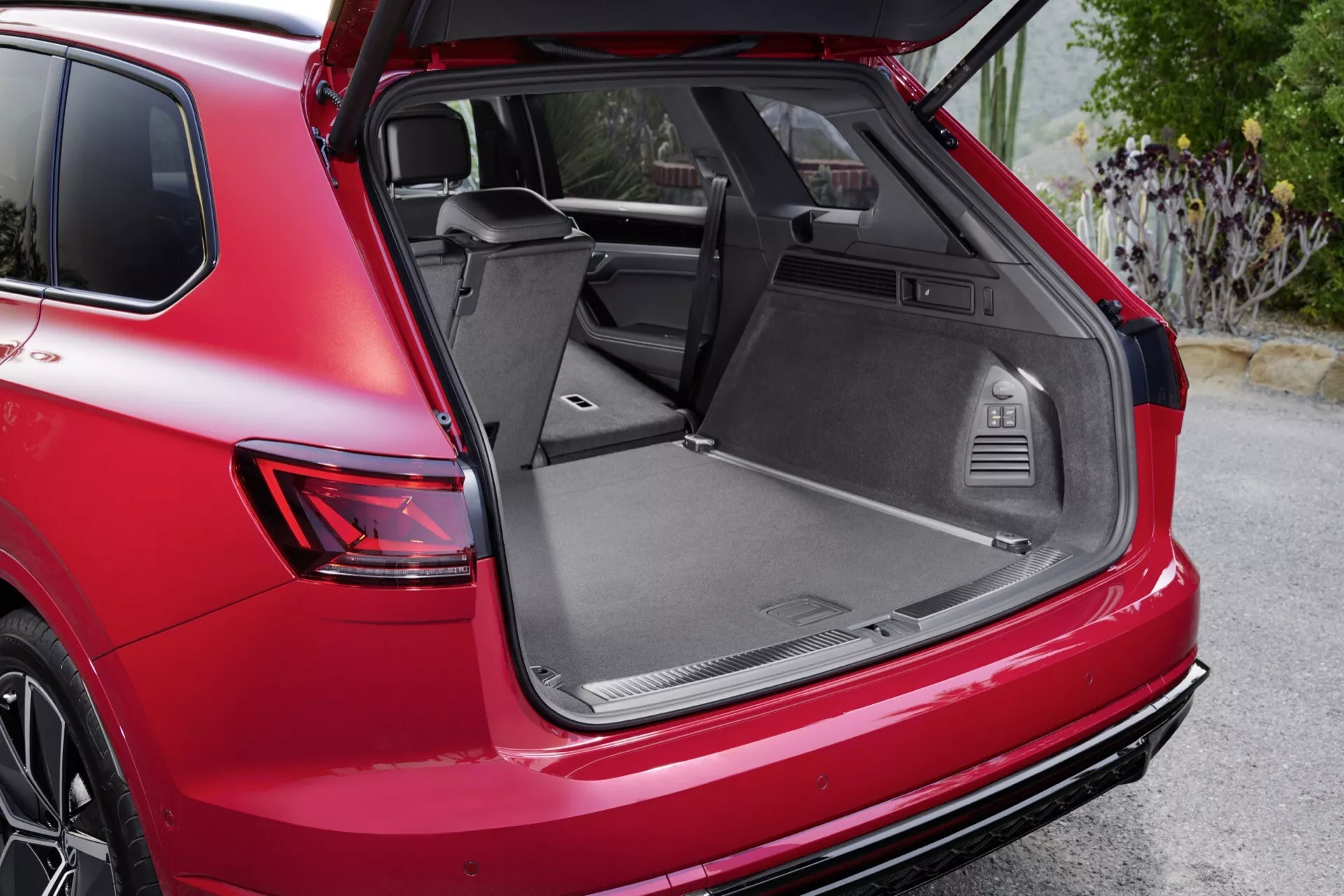 Czerwone SUV VW Touareg (III Facelift) z 2023 roku, widok z boku na tylną część z otwartym bagażnikiem, tylną stroną pasażera, światłem tylnym, kołem ze stopu, tylnym zderzakiem i przestronną przestrzenią ładunkową z funkcjami użytkowymi