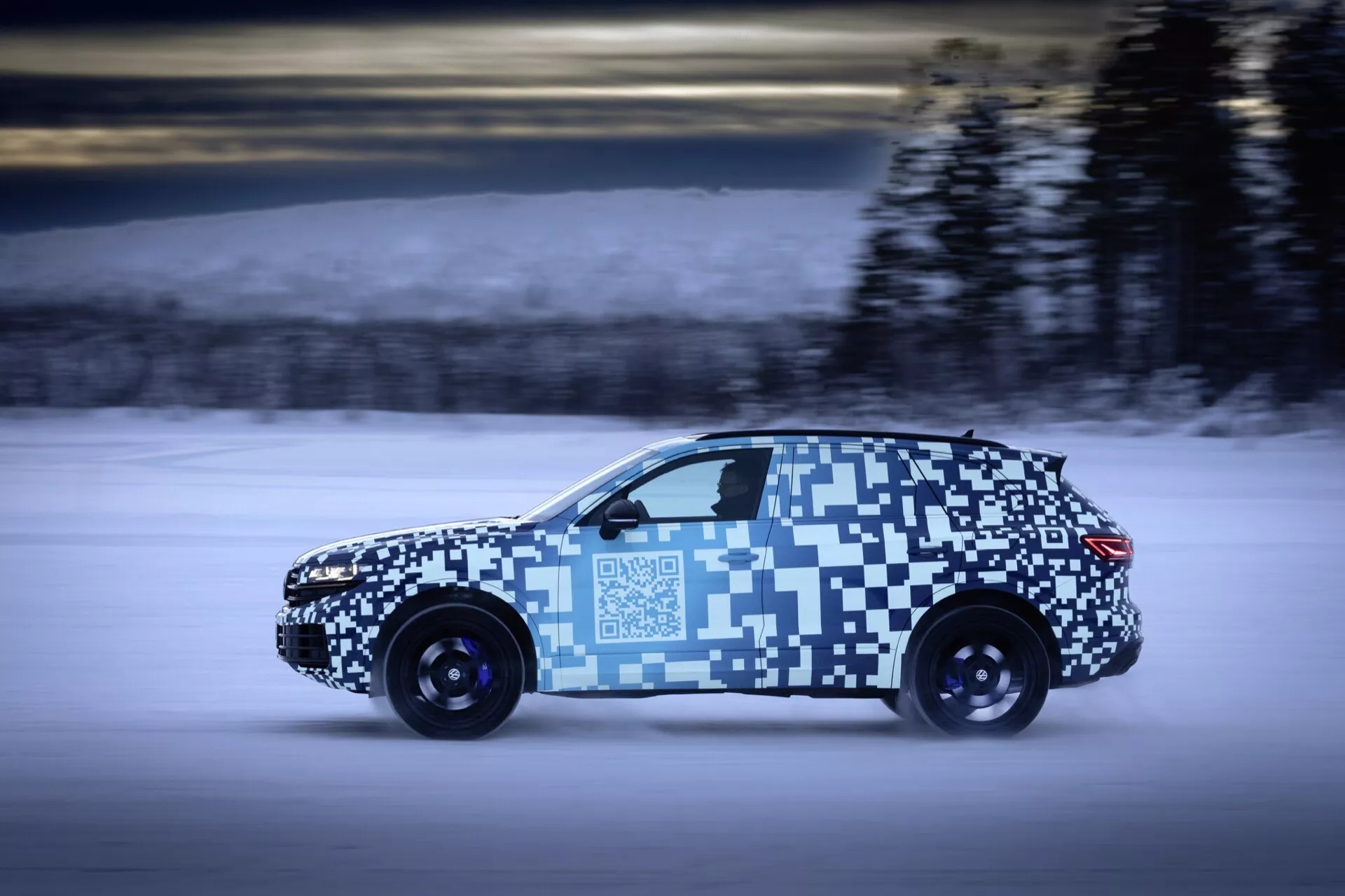 VW Touareg 2023 (III lifting) w ruchu, widok z boku z kamuflażem na śnieżnym krajobrazie, podkreślając dynamikę i potencjalny napęd na wszystkie koła