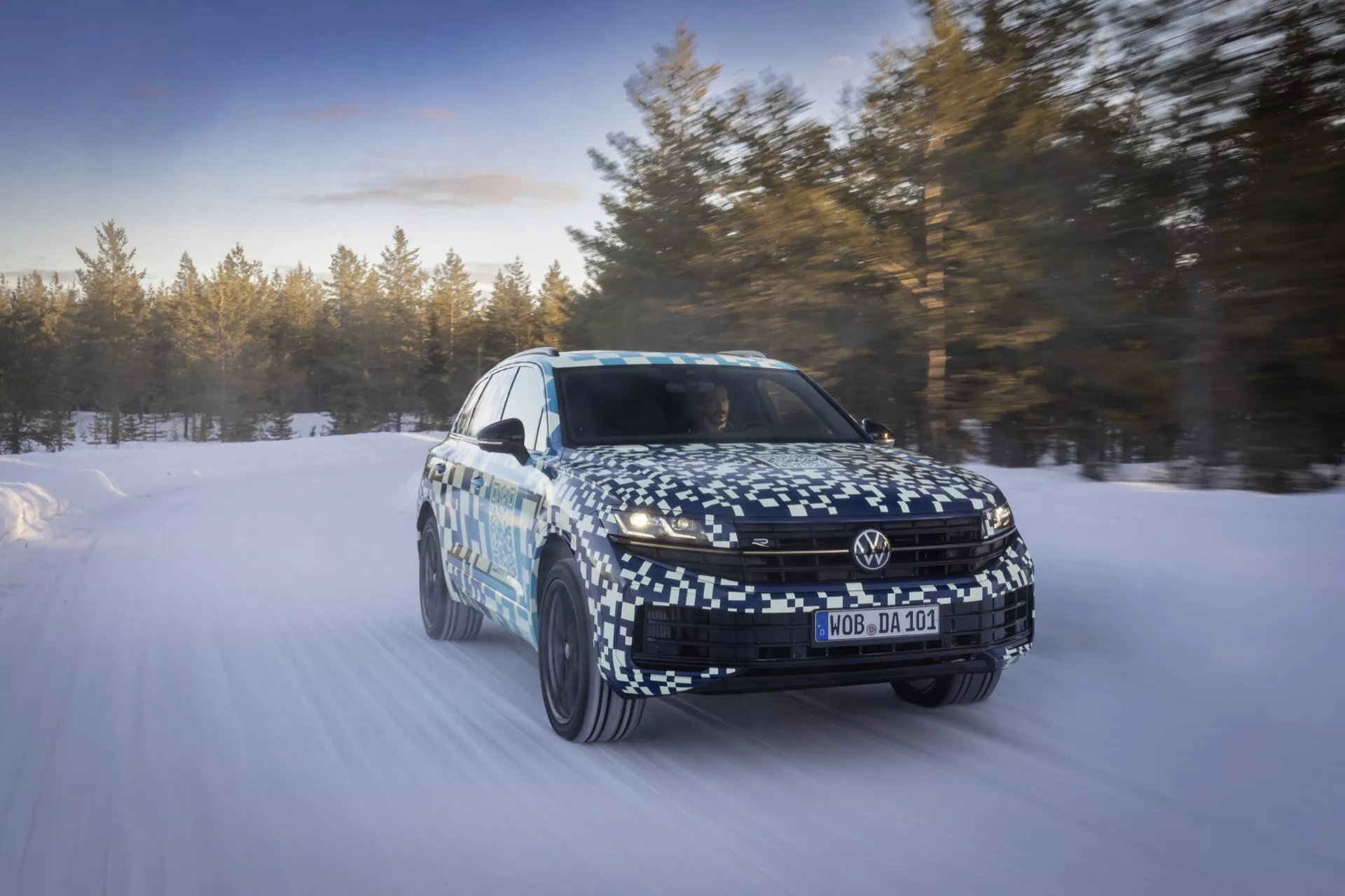 Model VW Touareg III Facelift 2023 uchwycony w ruchu na śnieżnym krajobrazie, prezentujący dynamiczną zdolność i zaawansowane funkcje technologiczne z perspektywy trzech czwartych z przodu