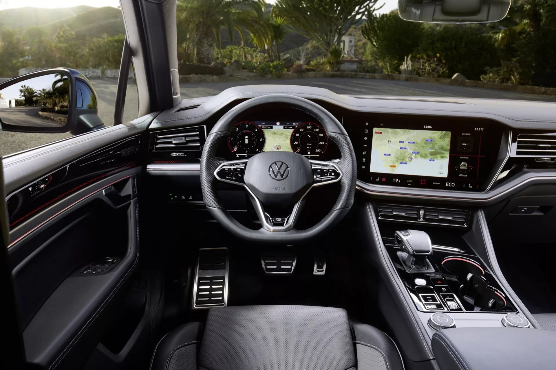 Wnętrze VW Touareg 2023 z widokiem na wielofunkcyjną kierownicę pokrytą skórą z logo Volkswagen, cyfrową deskę rozdzielczą, ekran dotykowy systemu infotainment i elegancki selektor biegów w luksusowym otoczeniu z ciemnymi tonami i metalowymi akcentami