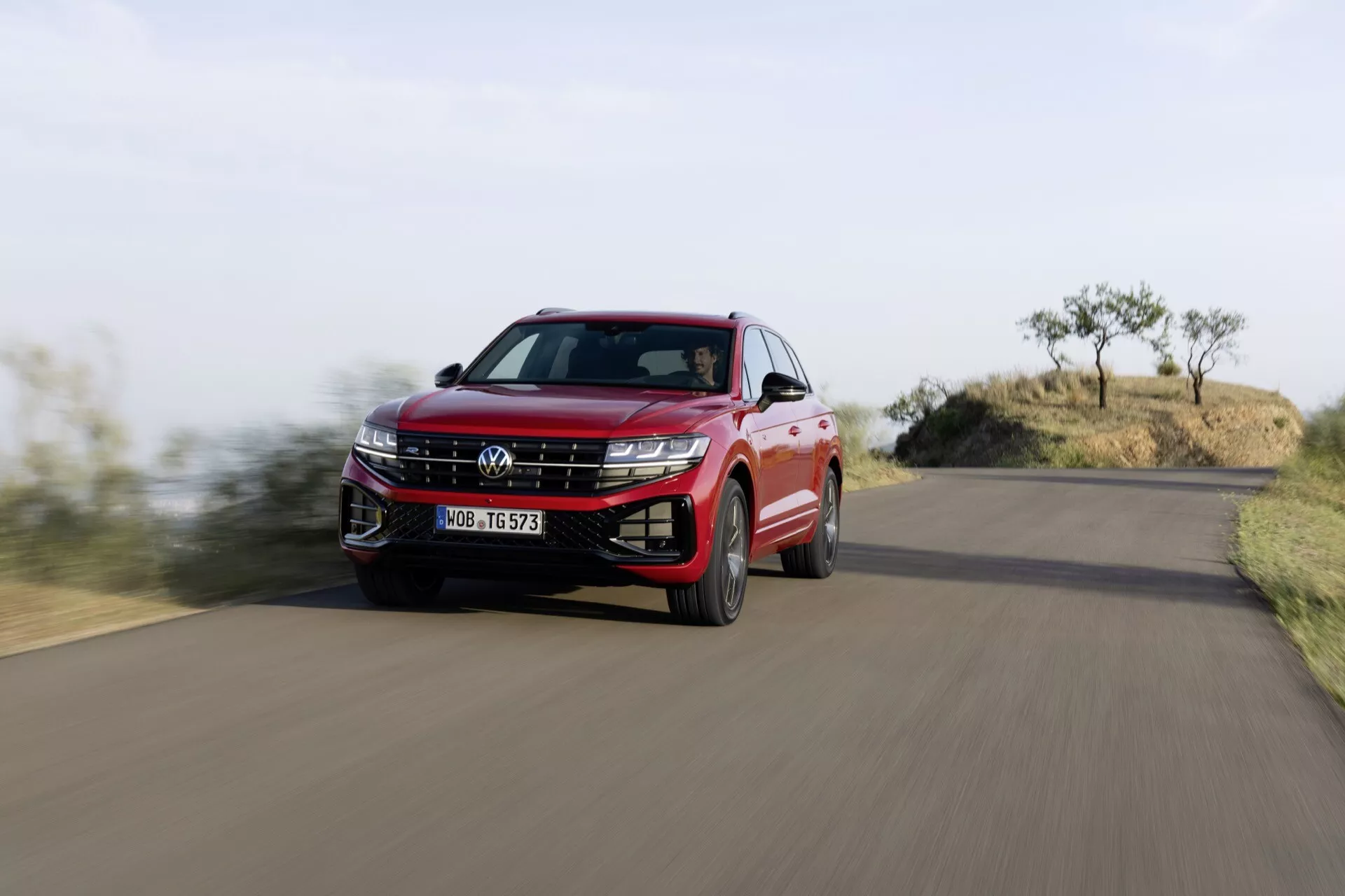 Volkswagen Touareg z roku 2023 w kolorze czerwonym, uchwycony w ruchu z niskiego kąta podkreślający grill, reflektory LED i dynamiczny profil boczny na tle krajobrazu naturalnego.