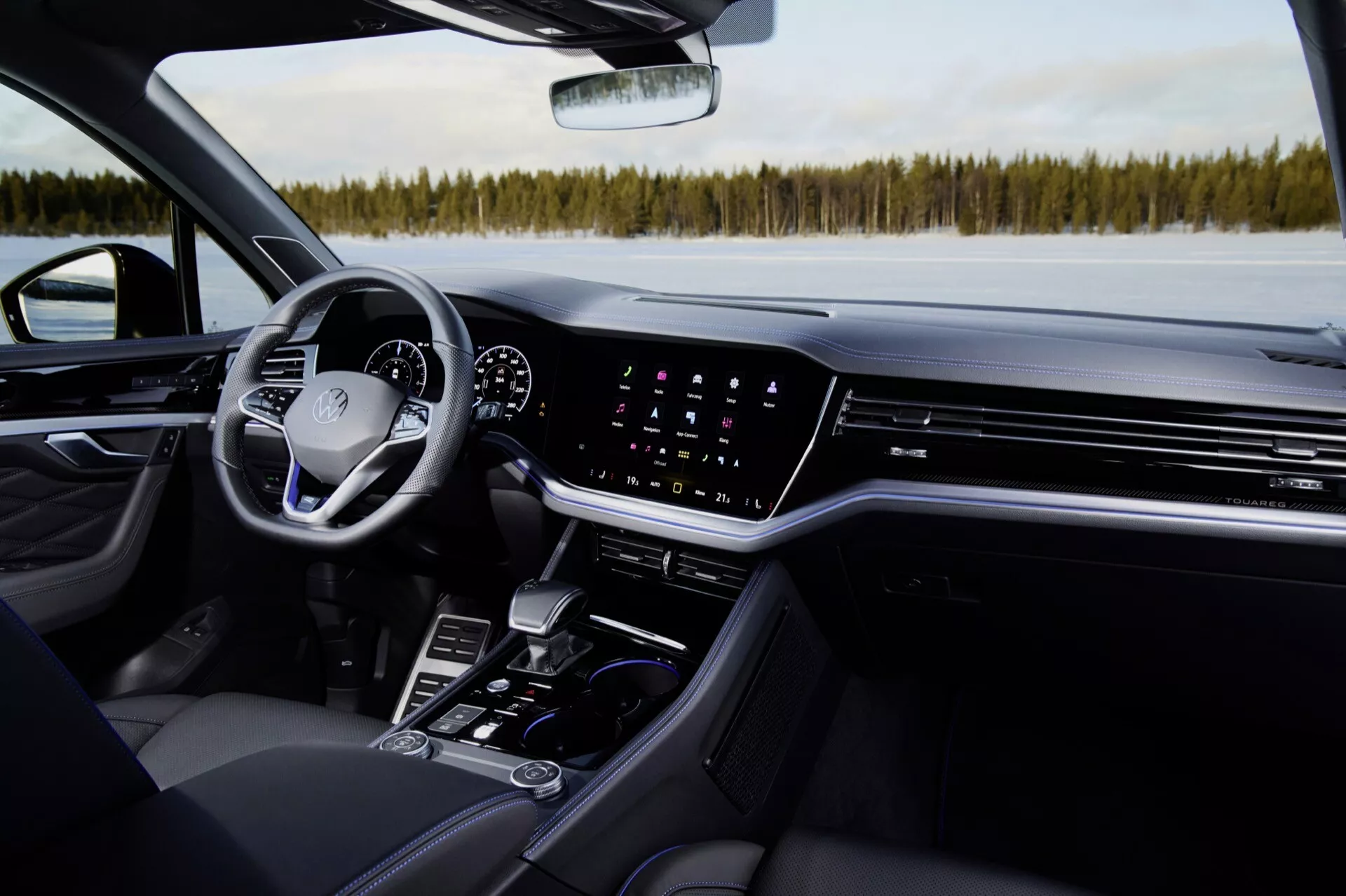 Wnętrze Volkswagen Touareg 2023: Perspektywa od strony pasażera podkreślająca deskę rozdzielczą, ekran dotykowy systemu infotainment, kontrolę klimatyzacji, cyfrowy panel instrumentów, wielofunkcyjną kierownicę i funkcje konsoli środkowej we współczesnym luksusowym samochodzie